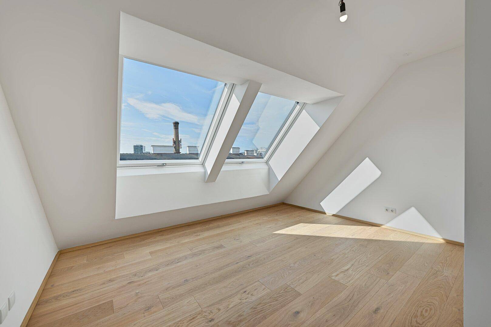 Heller Raum im Dachgeschoss mit Holzboden und großen Dachfenstern, bietet viel Tageslicht.