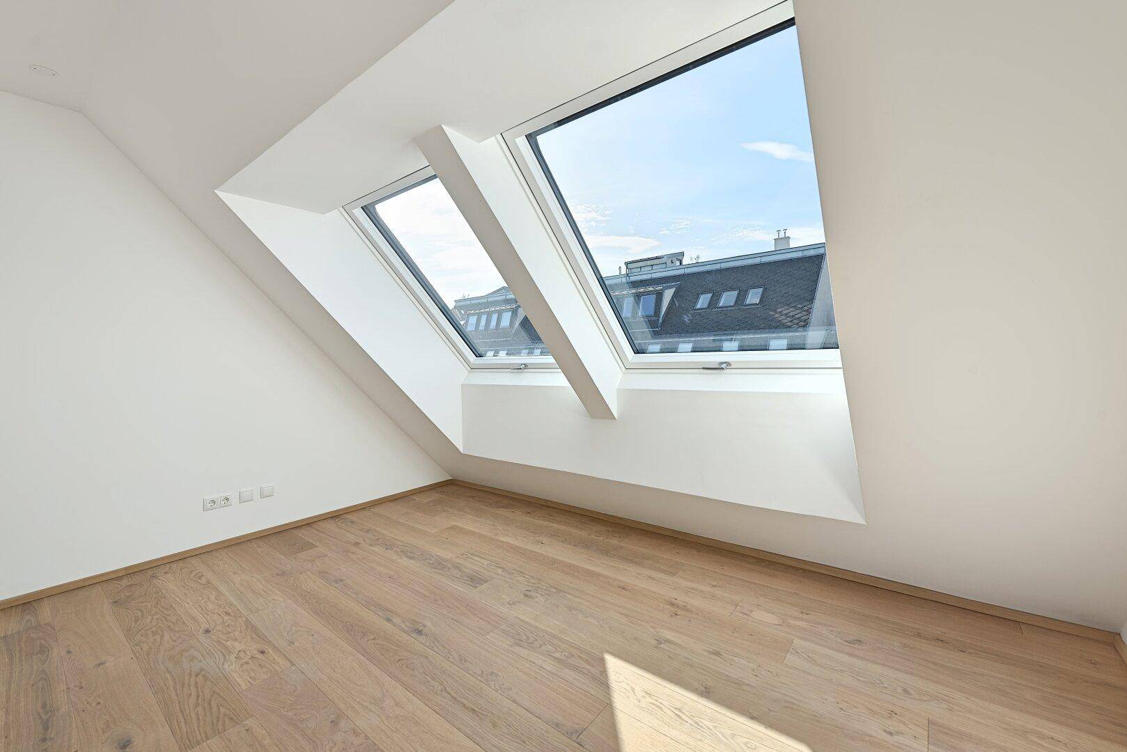 Lichtdurchfluteter Raum mit Holzboden und schrägen Wänden, ideal für ein Schlafzimmer oder Büro.