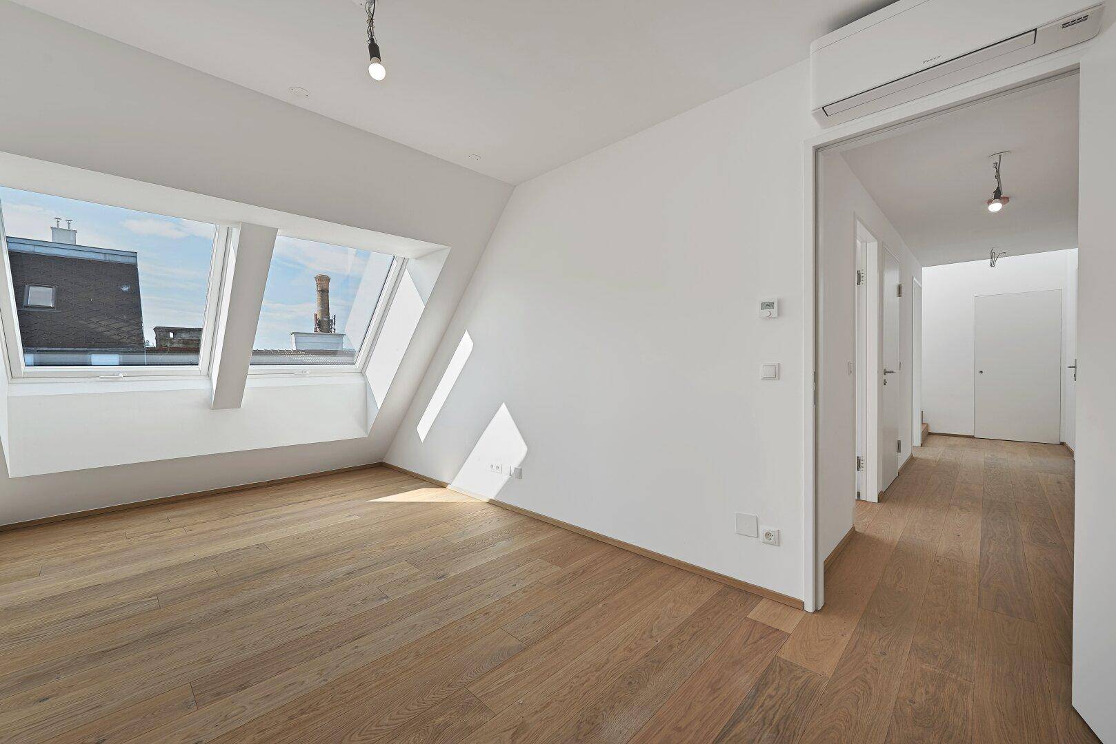 Geräumiger, heller Raum mit Holzboden, Dachfenstern und Klimaanlage, bietet flexible Nutzungsmöglichkeiten.