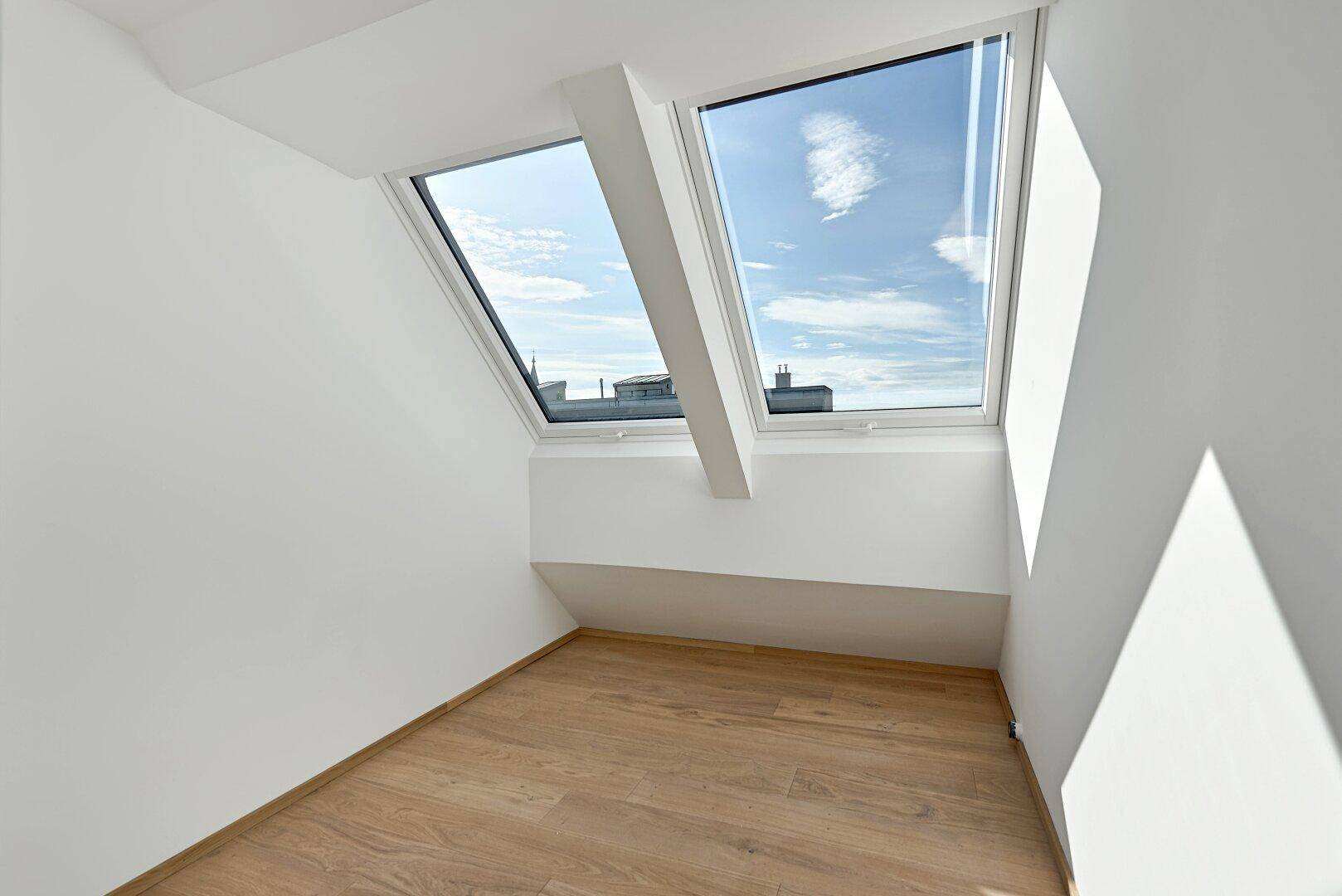 Kleiner, heller Raum im Dachgeschoss mit Holzboden und zwei Dachfenstern, bietet viel Licht.