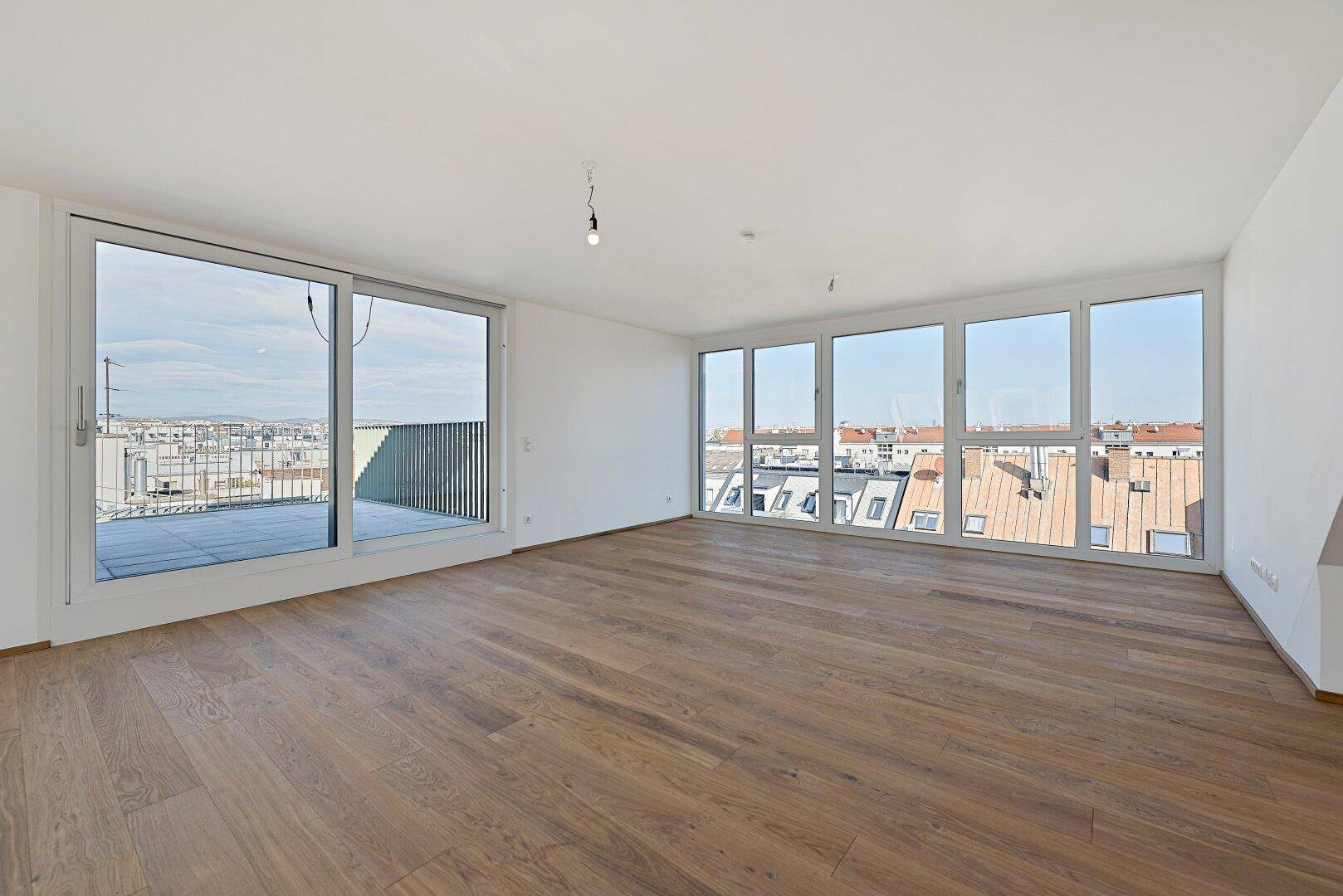 Großzügiger Wohnbereich mit Holzboden, raumhohen Fenstern und Zugang zur Dachterrasse.