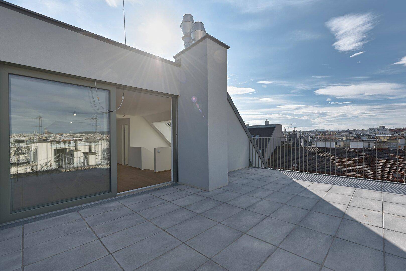 Sonniger Zugang zur Dachterrasse mit Schiebetür und Blick auf die Stadt.