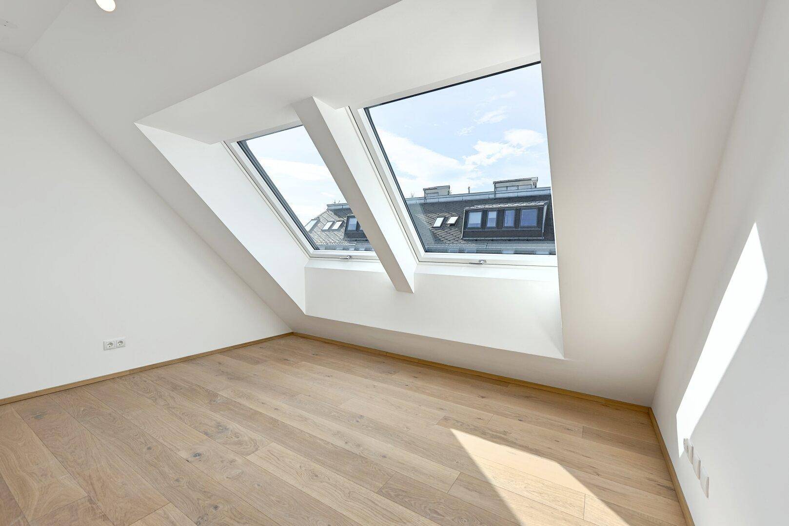Helles Zimmer im Dachgeschoss mit schrägen Wänden und großen Dachfenstern, bietet viel Tageslicht.