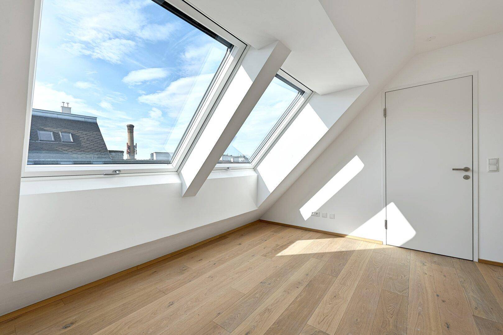 Lichtdurchfluteter Raum mit Holzboden und schrägen Dachfenstern, ideal als Schlaf- oder Arbeitszimmer.