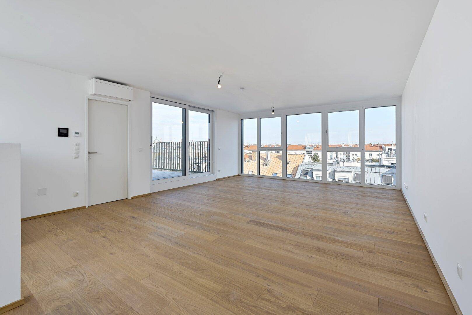 Geräumiger Wohnbereich mit großen Fenstern, Holzboden und direktem Zugang zur Außenterrasse.