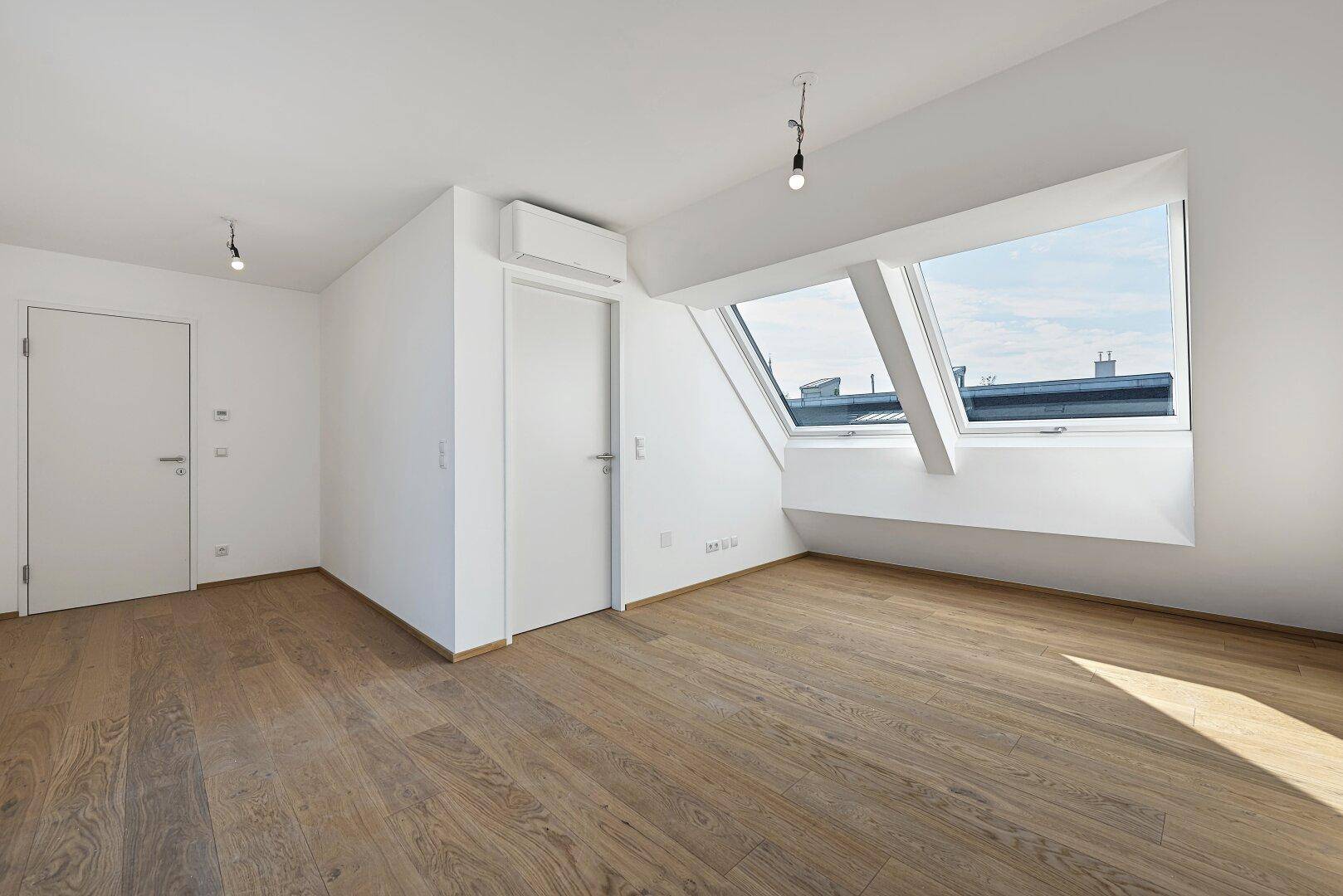 Helles Zimmer mit Holzboden, Dachfenstern und Klimaanlage, ideal als privater Rückzugsort.