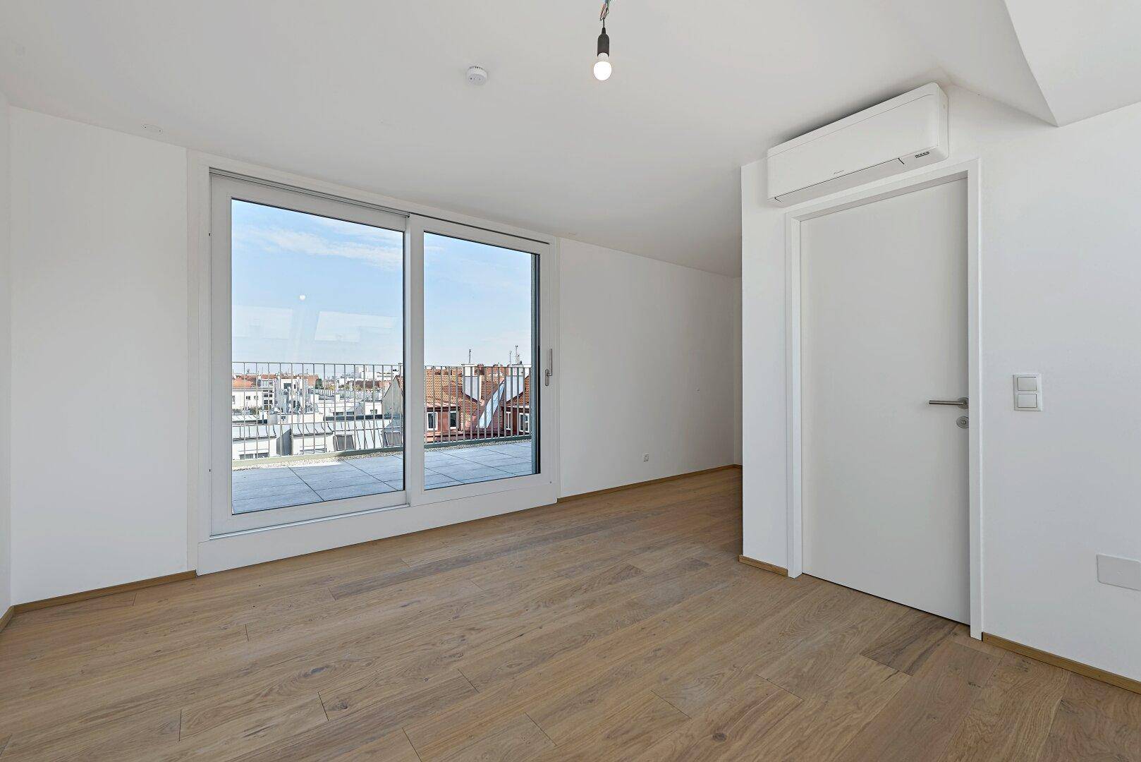 Geräumiger Wohnbereich mit Holzboden, Schiebetür zur Terrasse und integrierter Klimaanlage.