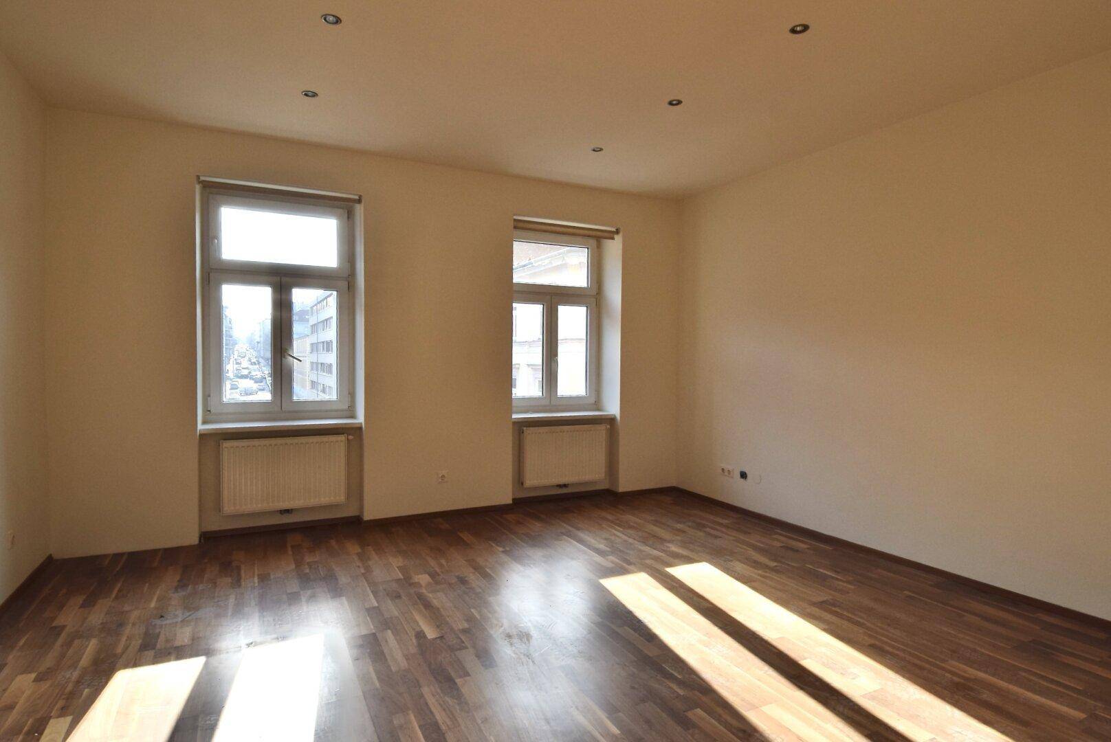 Lichtdurchfluteter Wohnraum mit elegantem Parkettboden und Blick auf die städtische Umgebung.