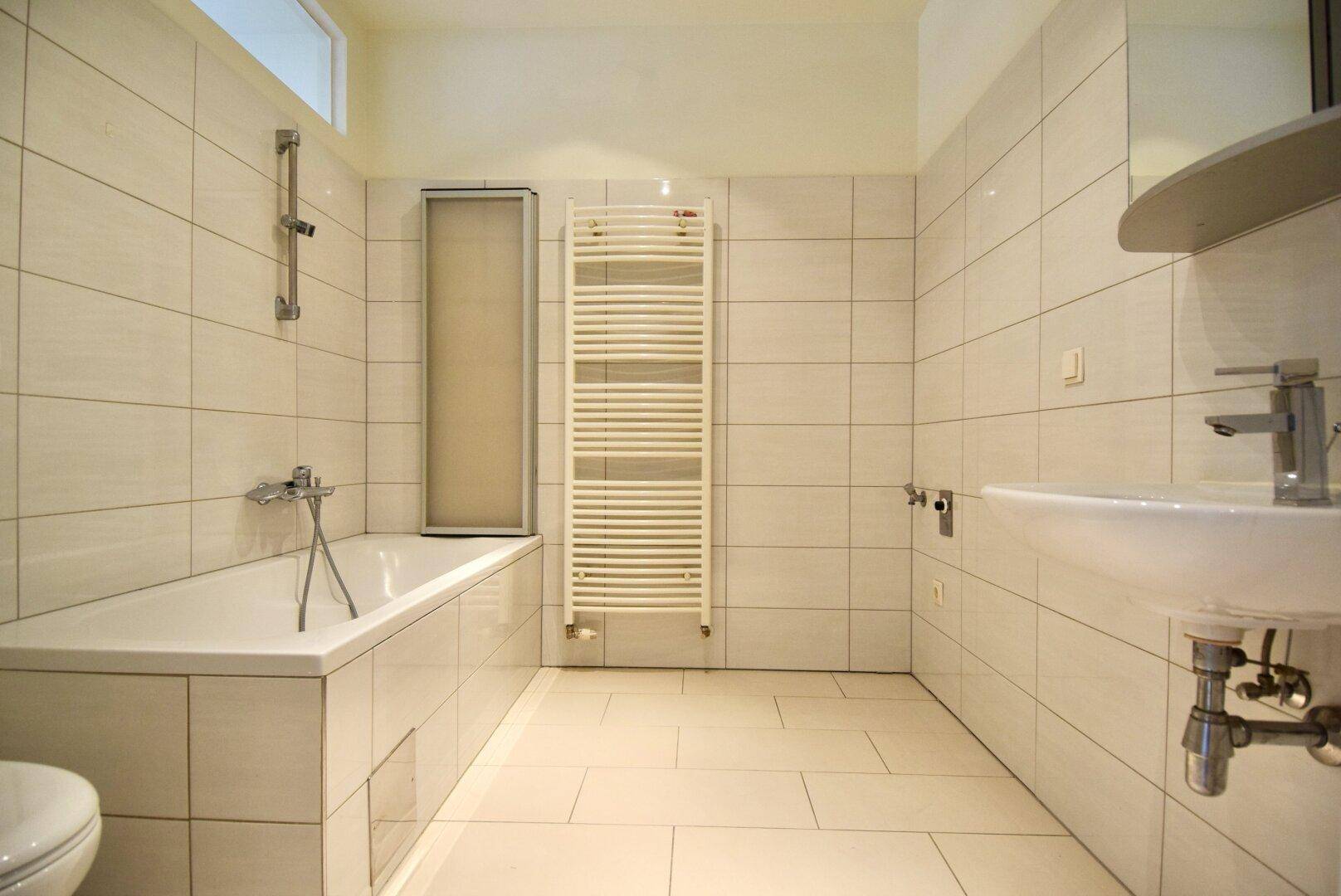 Helles Badezimmer mit Badewanne, Waschbecken, WC und einem praktischen Handtuchheizkörper.