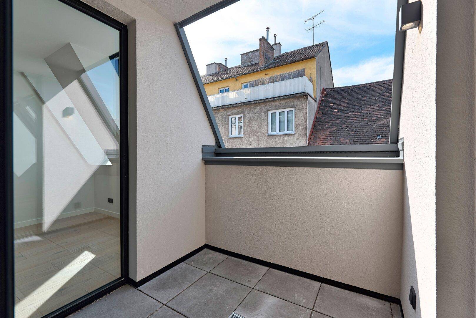 Kleiner Balkon mit Fliesenboden und Blick auf die umliegenden Gebäude in der Stadt.