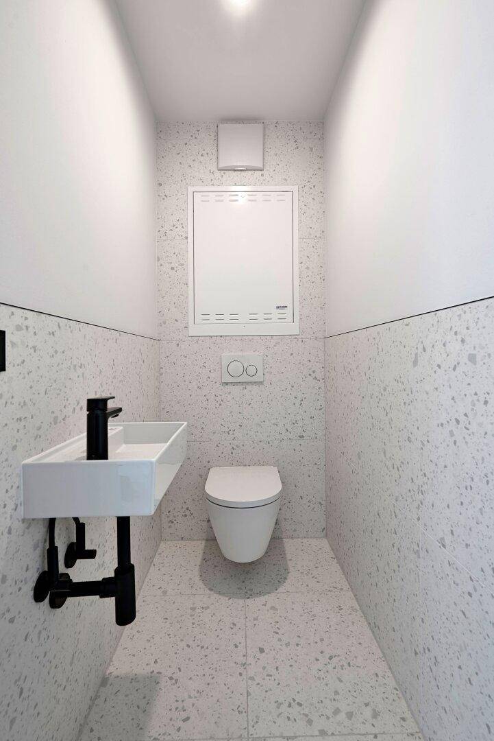 Modernes Gäste-WC mit Wand-WC, kleinem Waschbecken und Terrazzo-Fliesen in minimalistischem Design.