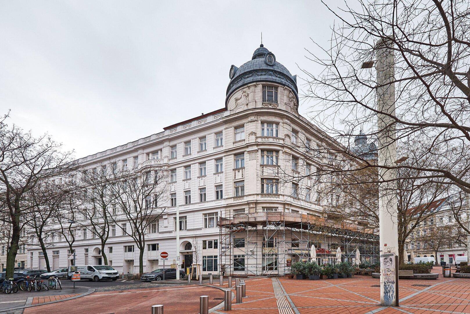 Historisches Gebäude mit Kuppel und Gerüst an der Fassade auf einem Stadtplatz.