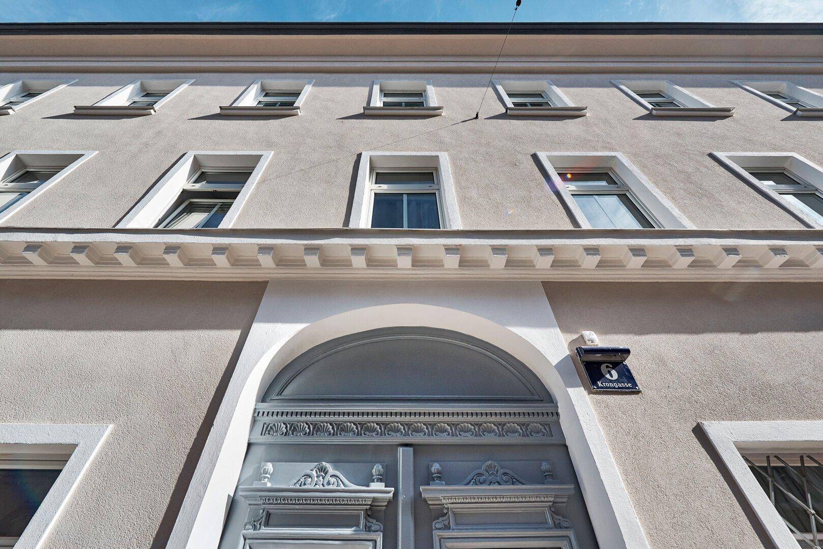 Fassade eines Altbaus mit zahlreichen Fenstern und einem verzierten Eingangsbereich unter blauem Himmel.