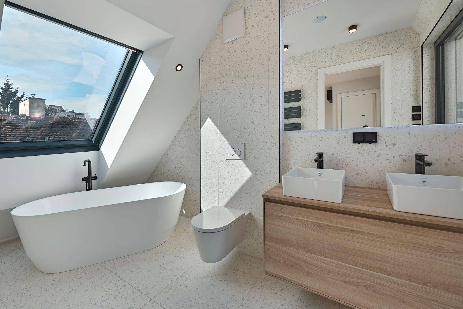 Modernes Badezimmer mit freistehender Badewanne, Doppelwaschbecken und großem Dachfenster für viel Tageslicht.