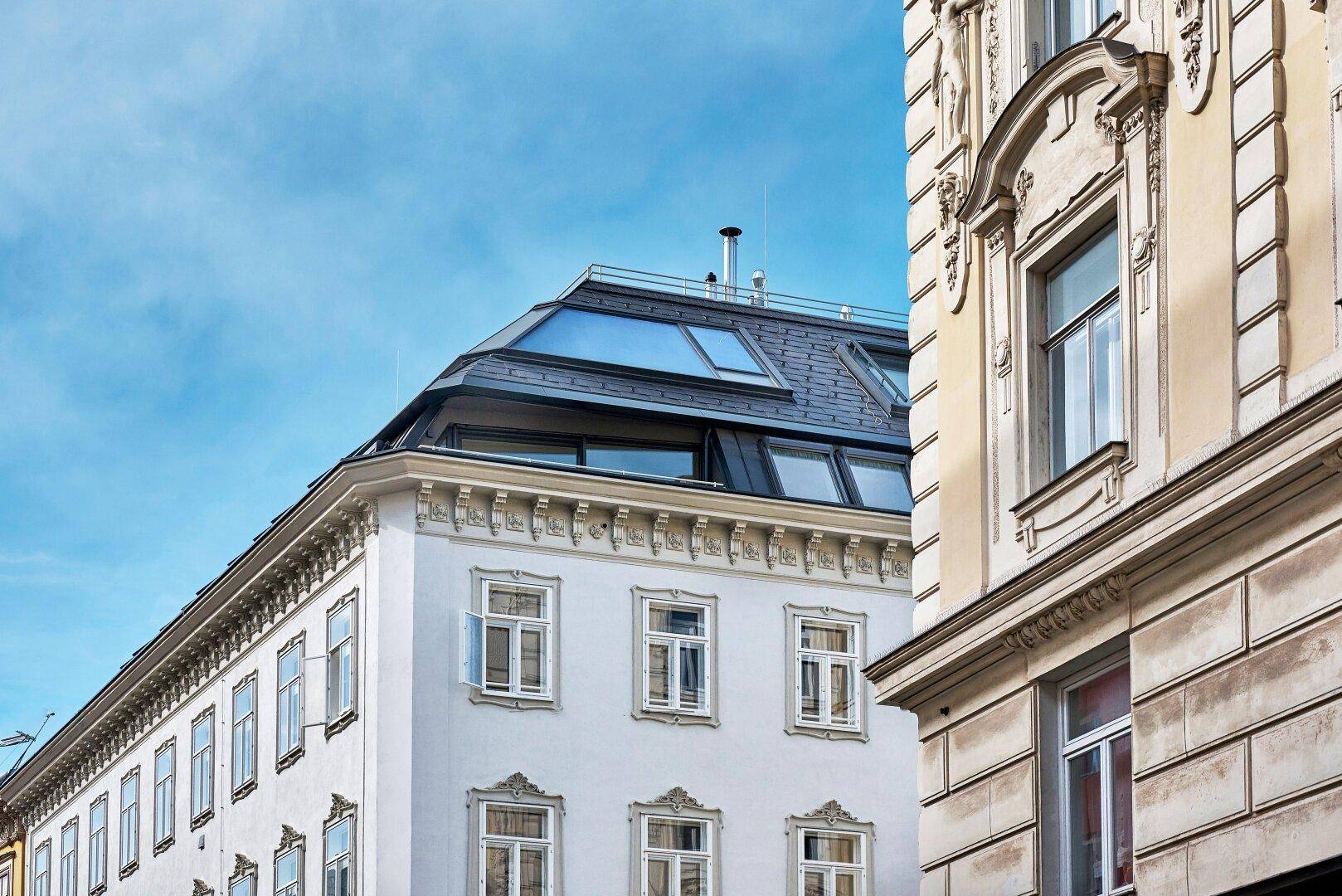 Dachbereich eines Gebäudes mit moderner Mansarddachkonstruktion und integrierten Dachfenstern unter klarem Himmel.