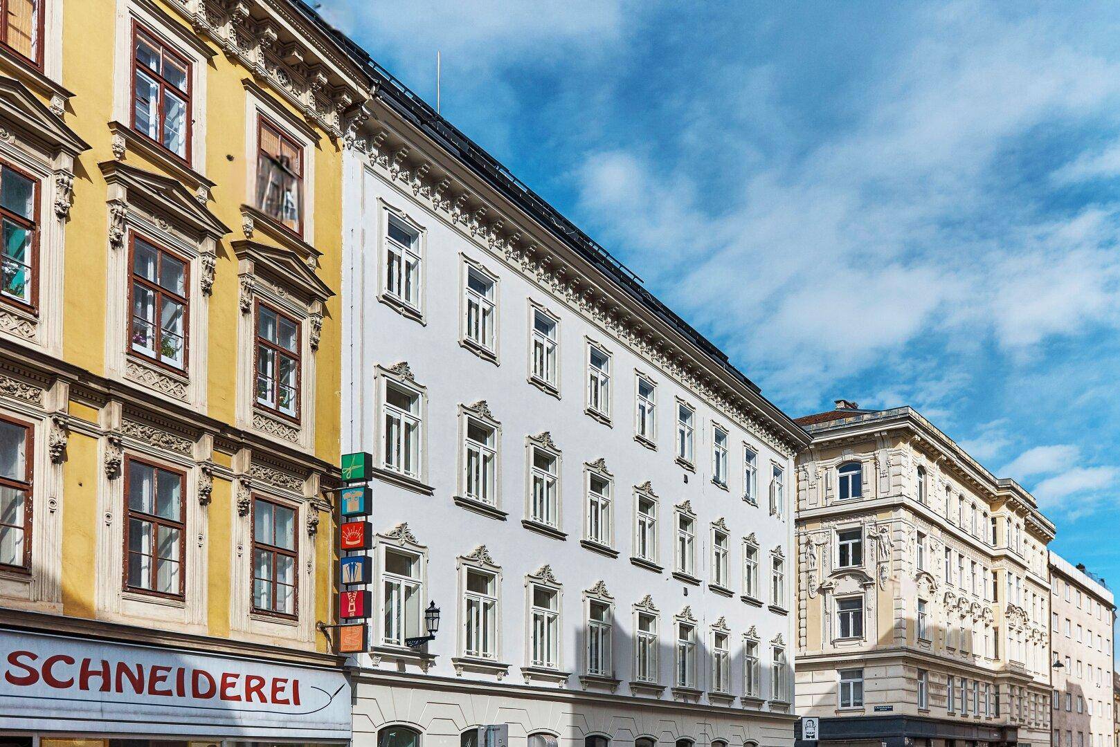 Historische Straßenzugansicht mit mehreren Altbauten, die unterschiedliche Fassadenfarben und architektonische Details zeigen.