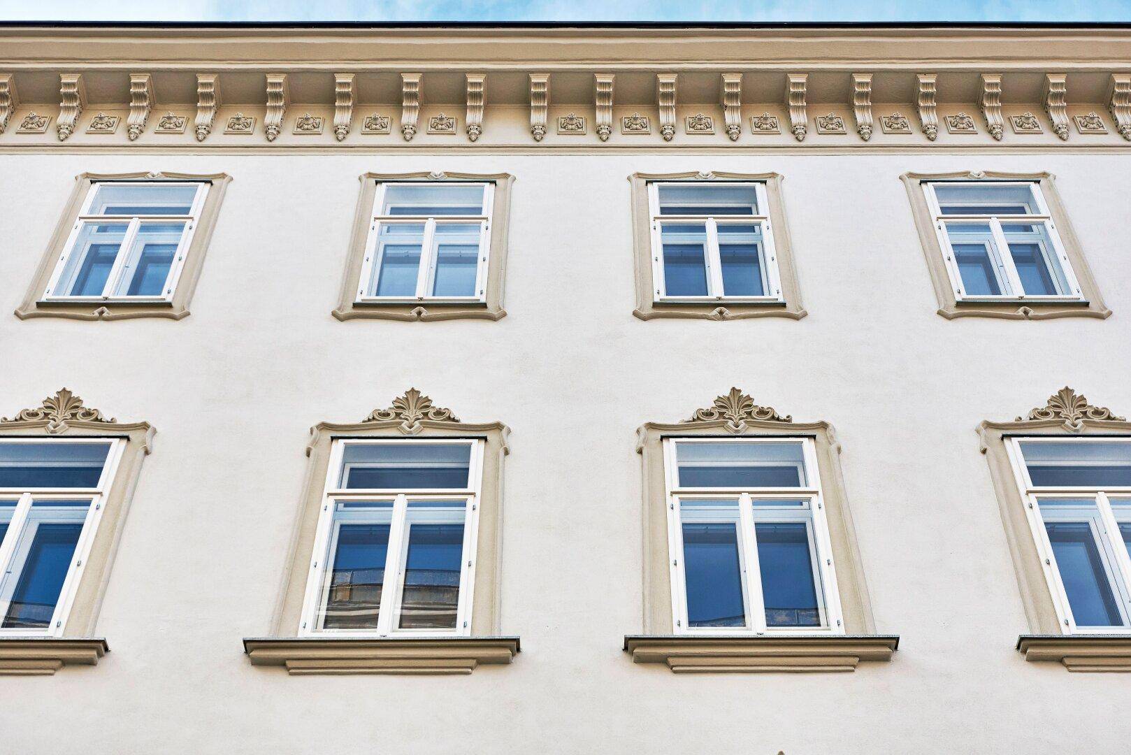 Nahaufnahme der eleganten Fassade mit verzierten Fenstern und Stuckelementen, die den klassischen Stil betonen.
