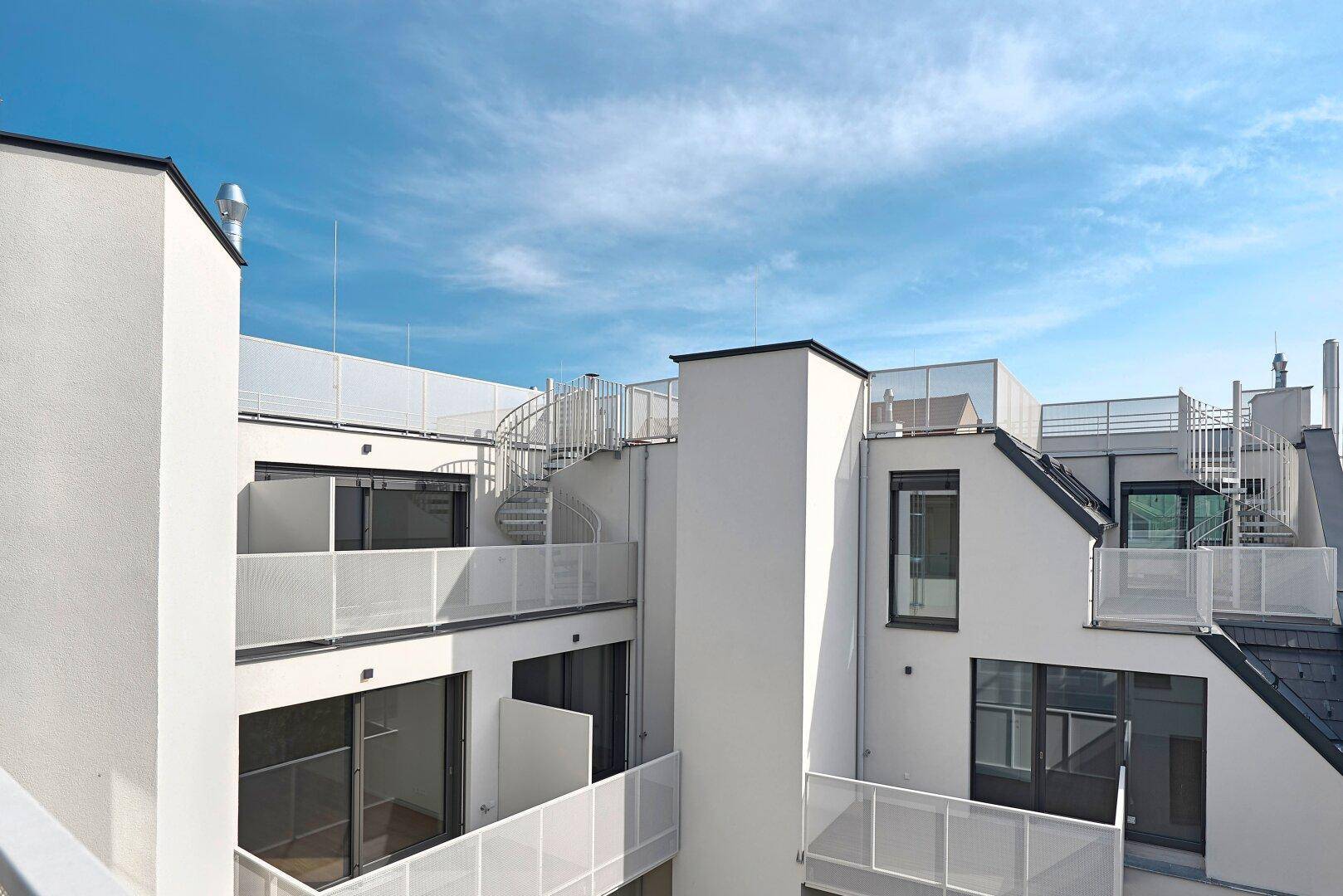 Moderne Dachterrassen und Balkone mit weißen Geländern und einer Wendeltreppe, die verschiedene Ebenen verbindet.