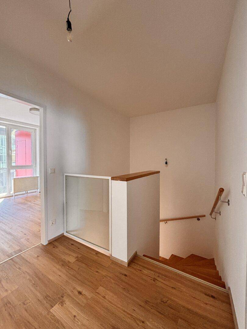 Heller Flurbereich mit Holzboden und Treppenabgang, ausgestattet mit Glasgeländer.