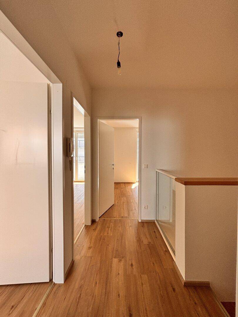 Geräumiger Flur mit Holzboden, der zu verschiedenen Zimmern und einem Treppenhaus führt.