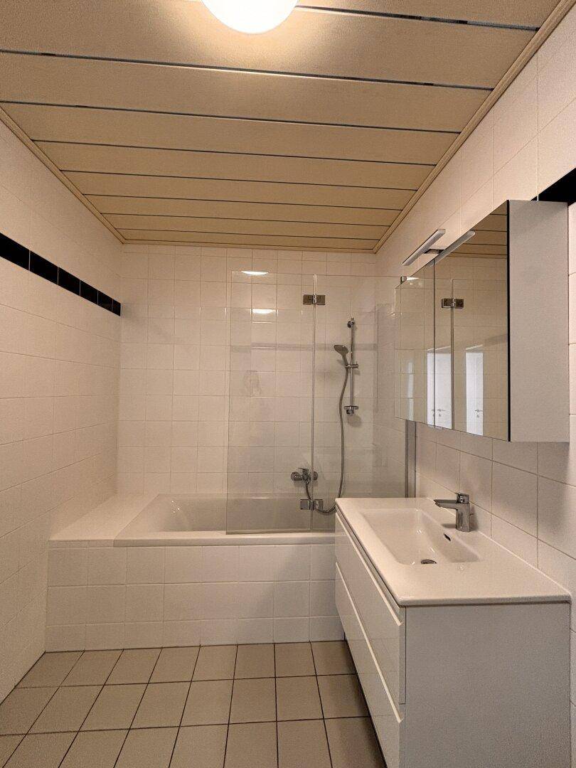 Modernes Badezimmer mit Badewanne, Dusche, Waschtisch und hellen Fliesen.