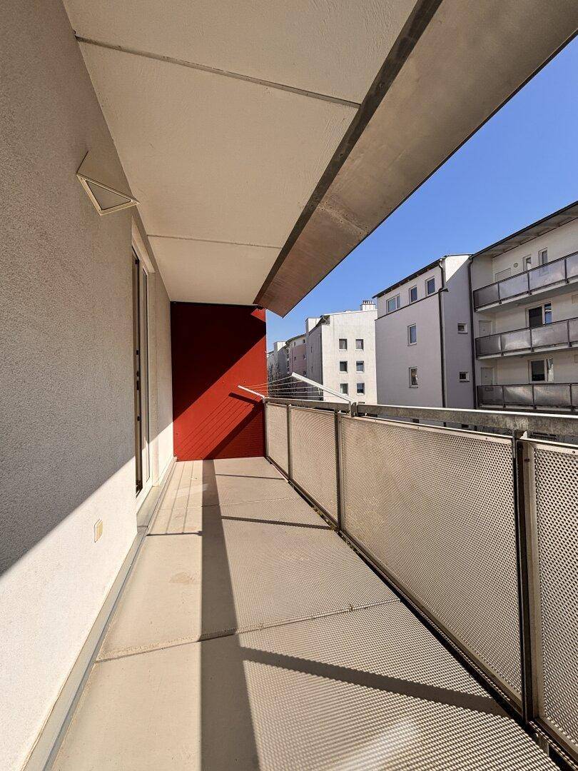 Langer, schmaler Balkon mit Metallgeländer und Blick auf die umliegenden Gebäude.