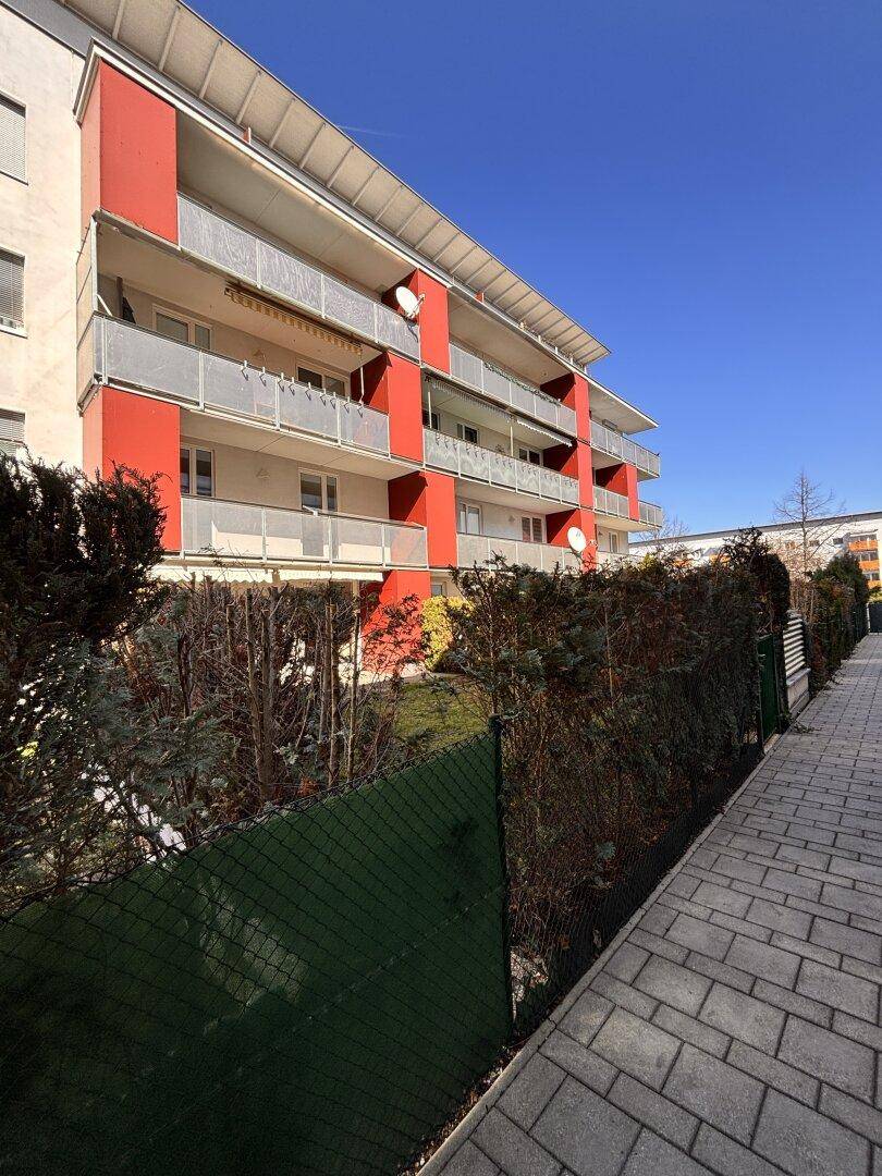 Modernes Wohngebäude mit roter Fassade, mehreren Balkonen und grüner Umgebung.