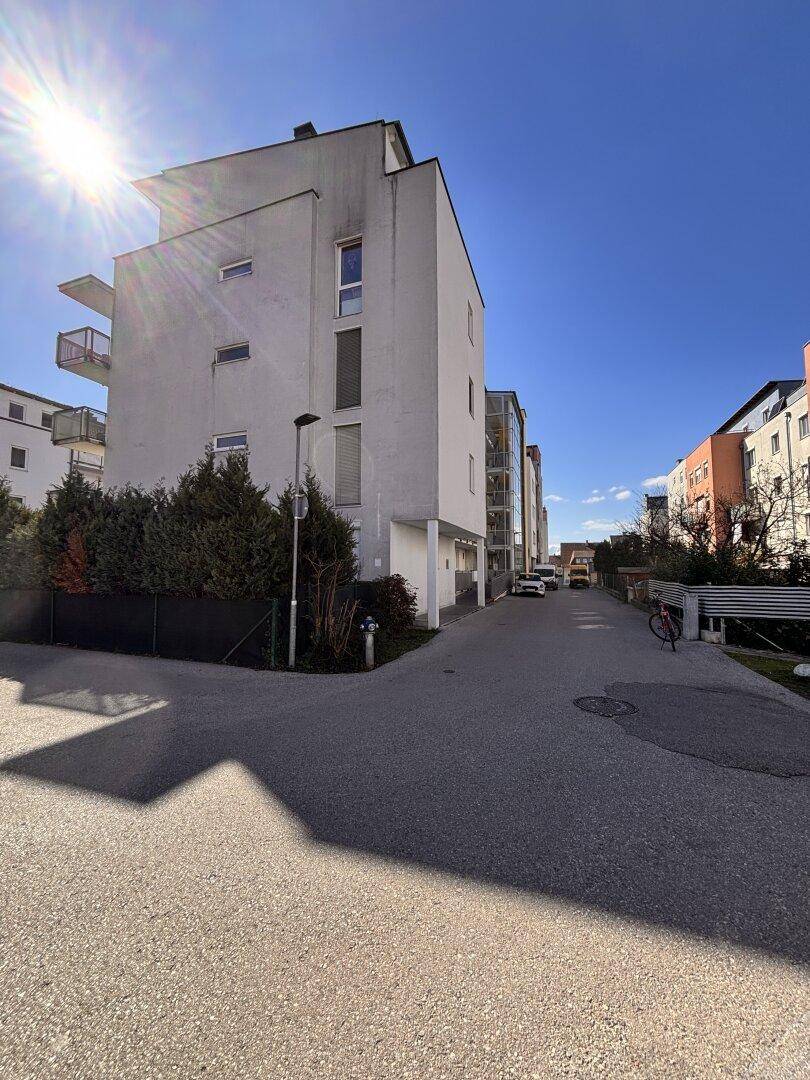 Weißes Wohngebäude mit Balkonen und Zufahrt an einem sonnigen Tag.