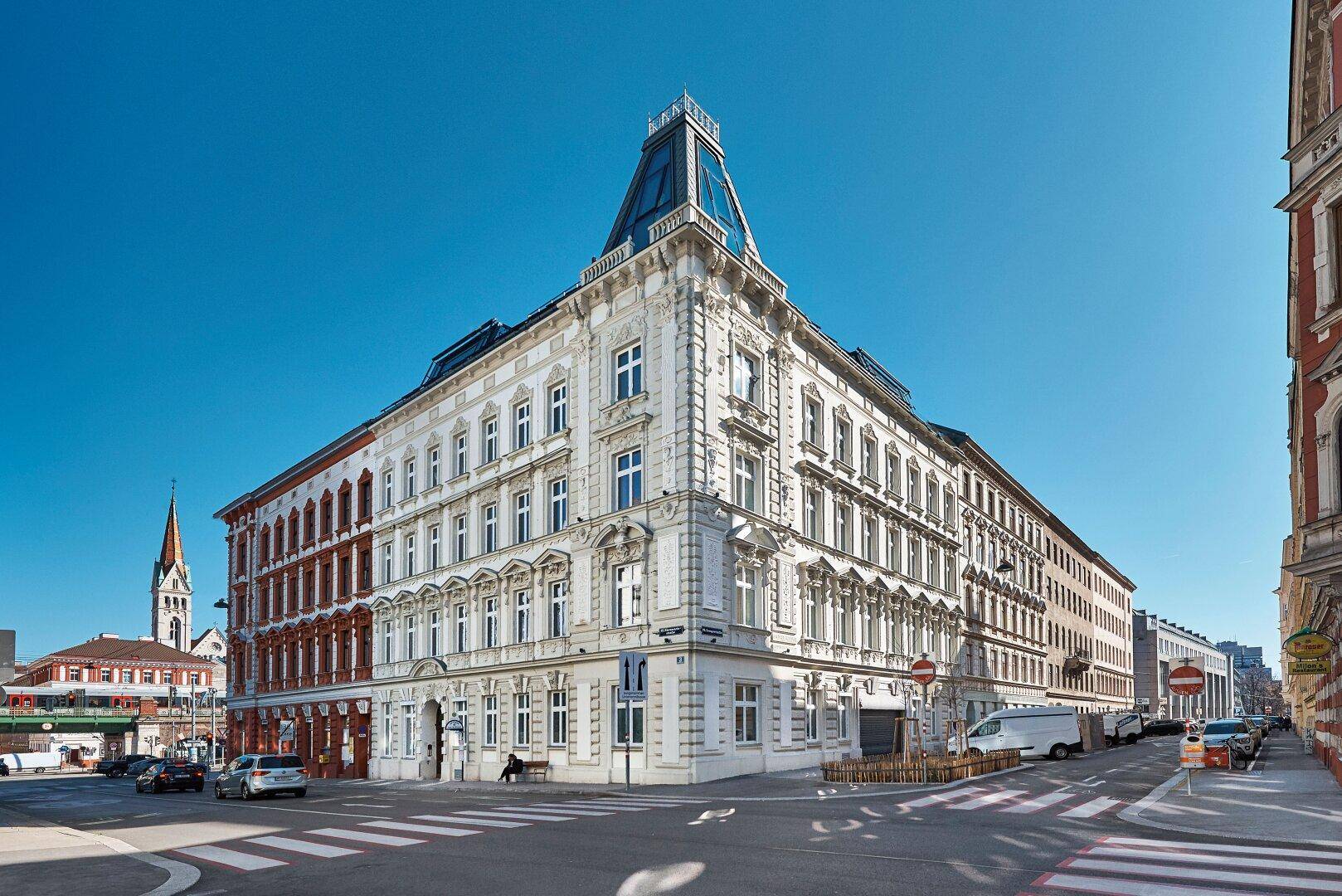 Historisches Eckgebäude mit modernem Dachausbau an einer belebten Straße.