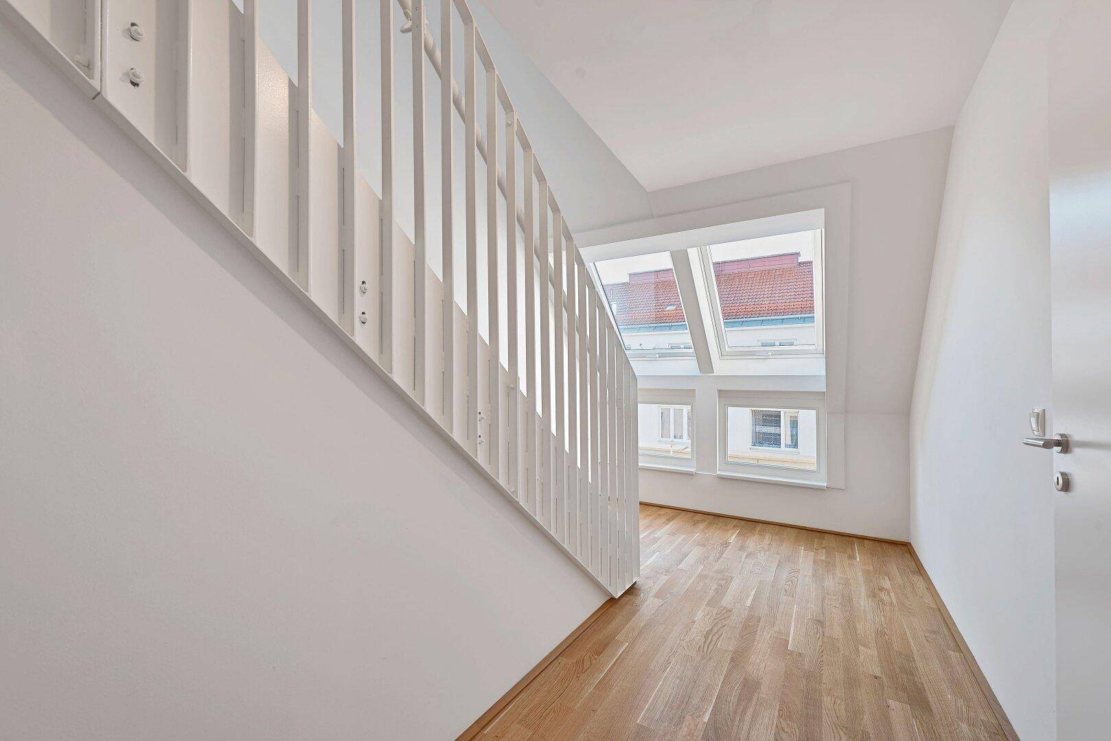 Moderner Treppenaufgang mit Holzstufen und großen Dachfenstern, die viel Licht hereinlassen.