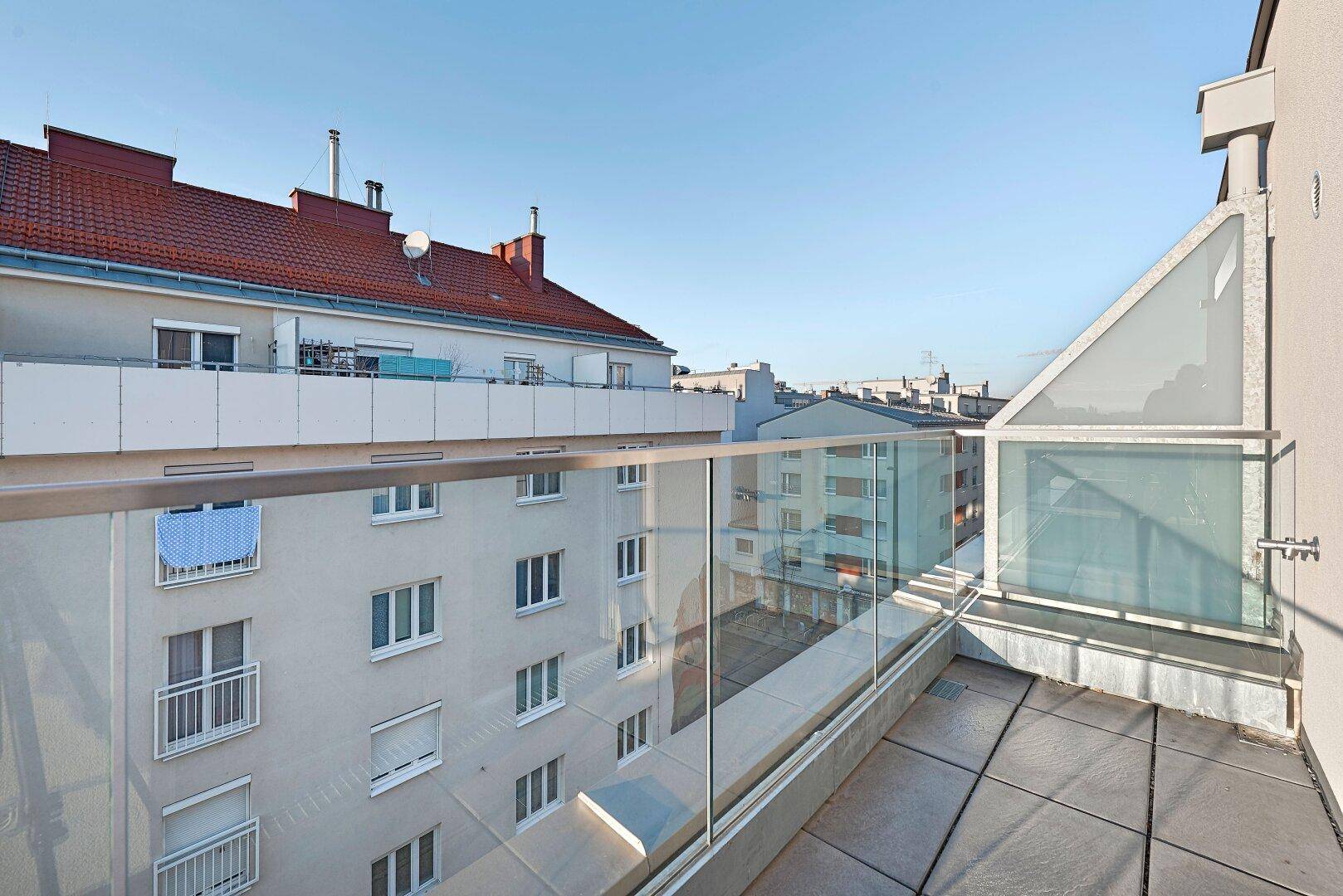 Dachterrasse mit modernem Glasgeländer und weitem Blick über die Dächer der Stadt.