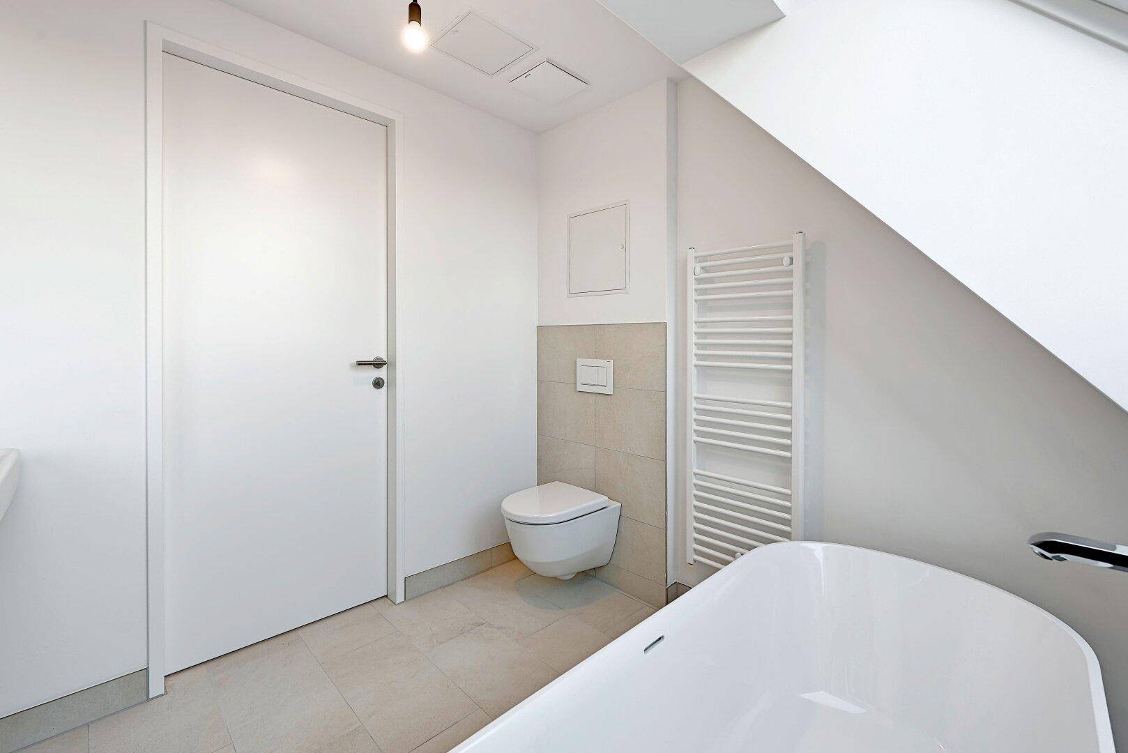 Modernes Badezimmer mit wandhängendem WC, beheiztem Handtuchhalter und hellen Fliesen.