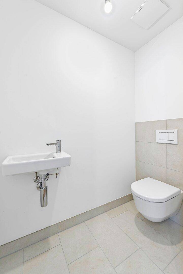 Modernes Gäste-WC mit wandhängendem WC und kleinem Waschbecken, hell gefliest.
