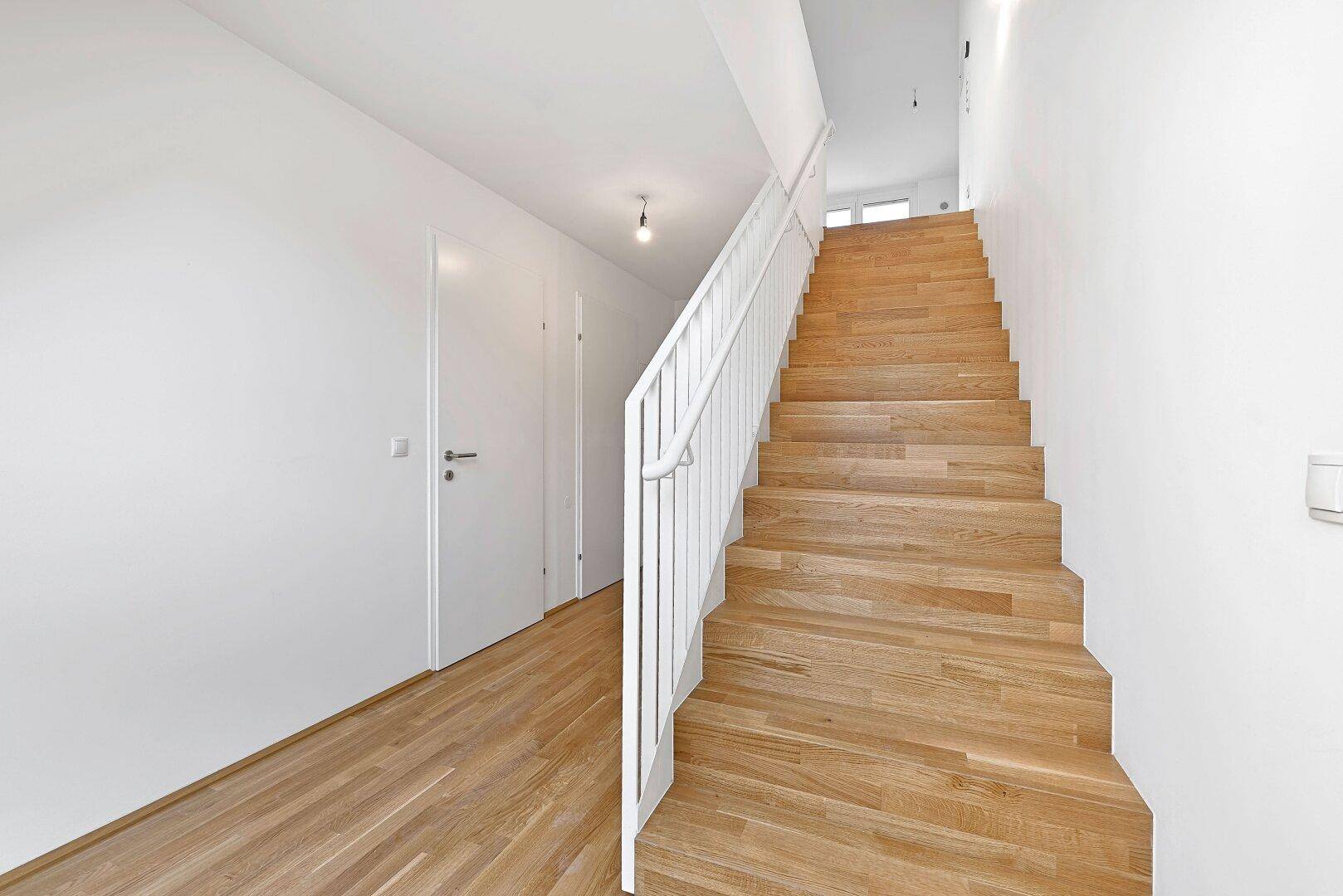 Geräumiger Flur mit eleganter Holztreppe und weißem Geländer, der zu den oberen Etagen führt.
