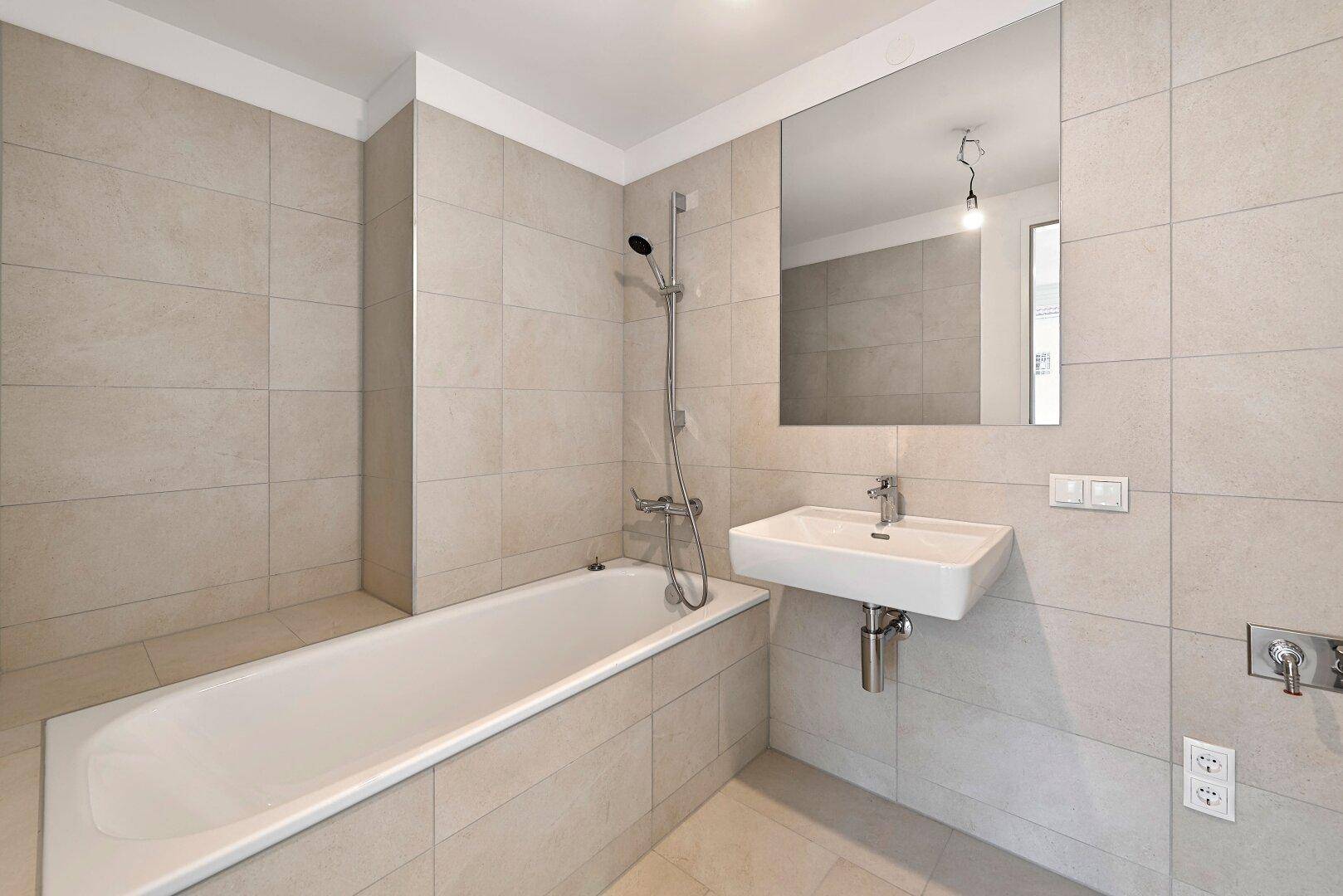Modernes Badezimmer mit Badewanne, Duschfunktion, Wandwaschbecken und großem Spiegel.