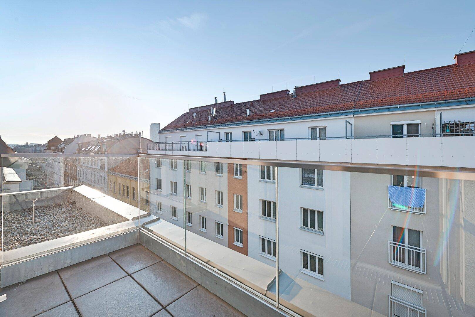 Weitläufige Dachterrasse mit Glasgeländer und Panoramablick über die Dächer der Stadt.
