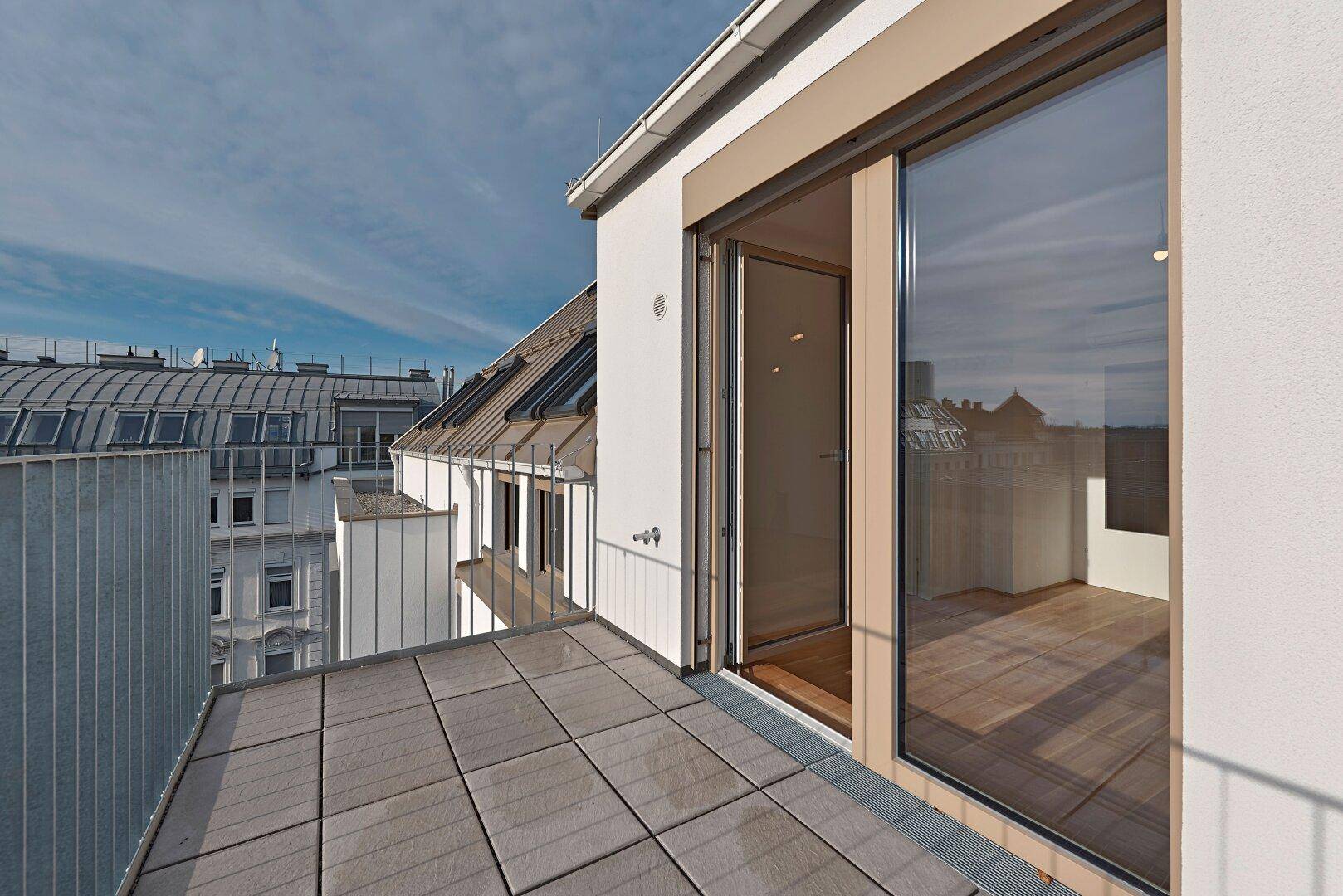 Heller Balkon mit Fliesenboden und großer Glastür, die in die Wohnung führt, mit Stadtblick.