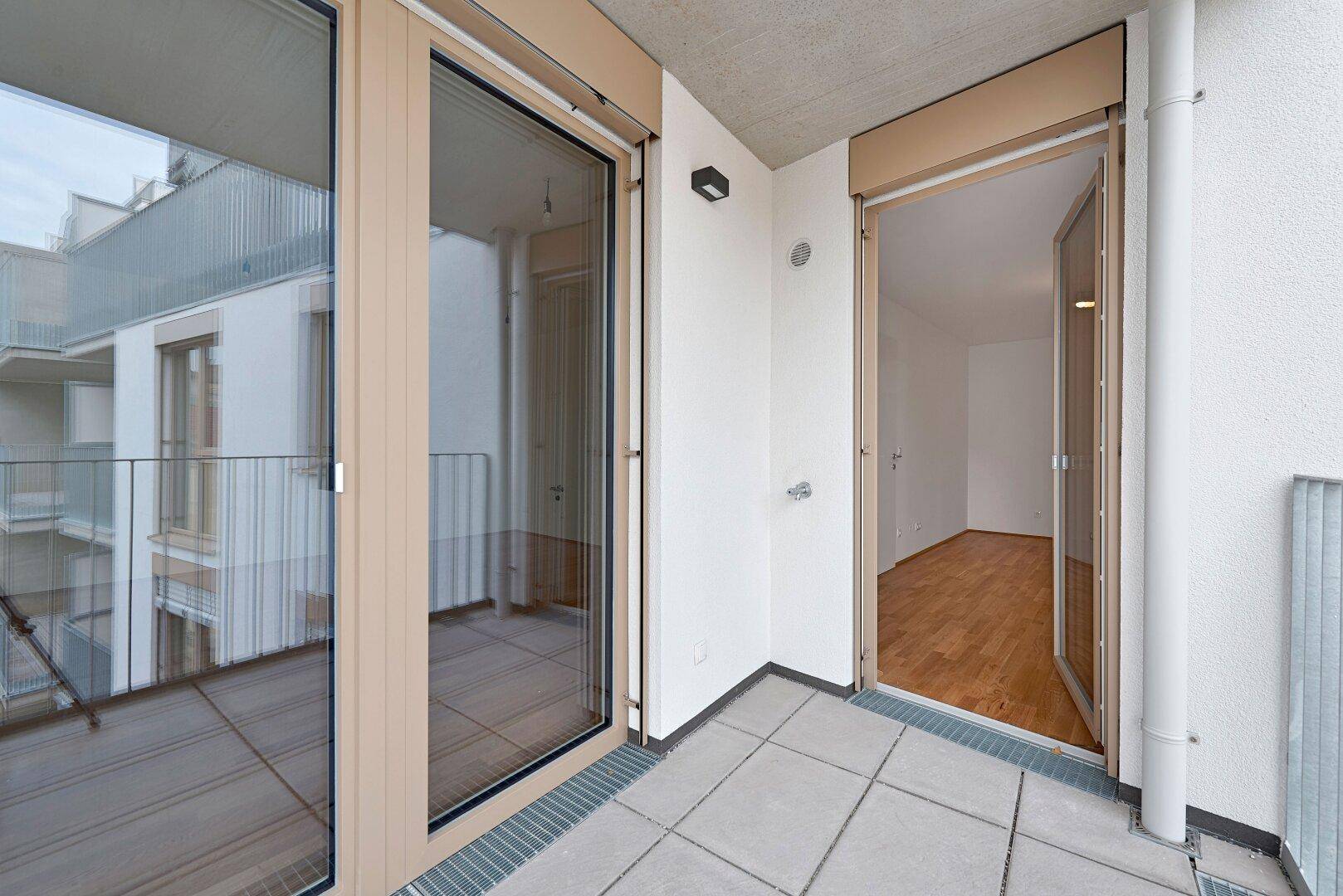 Geräumiger Balkon mit Fliesenboden und Blick auf den Innenhof, zugänglich vom Wohnbereich.