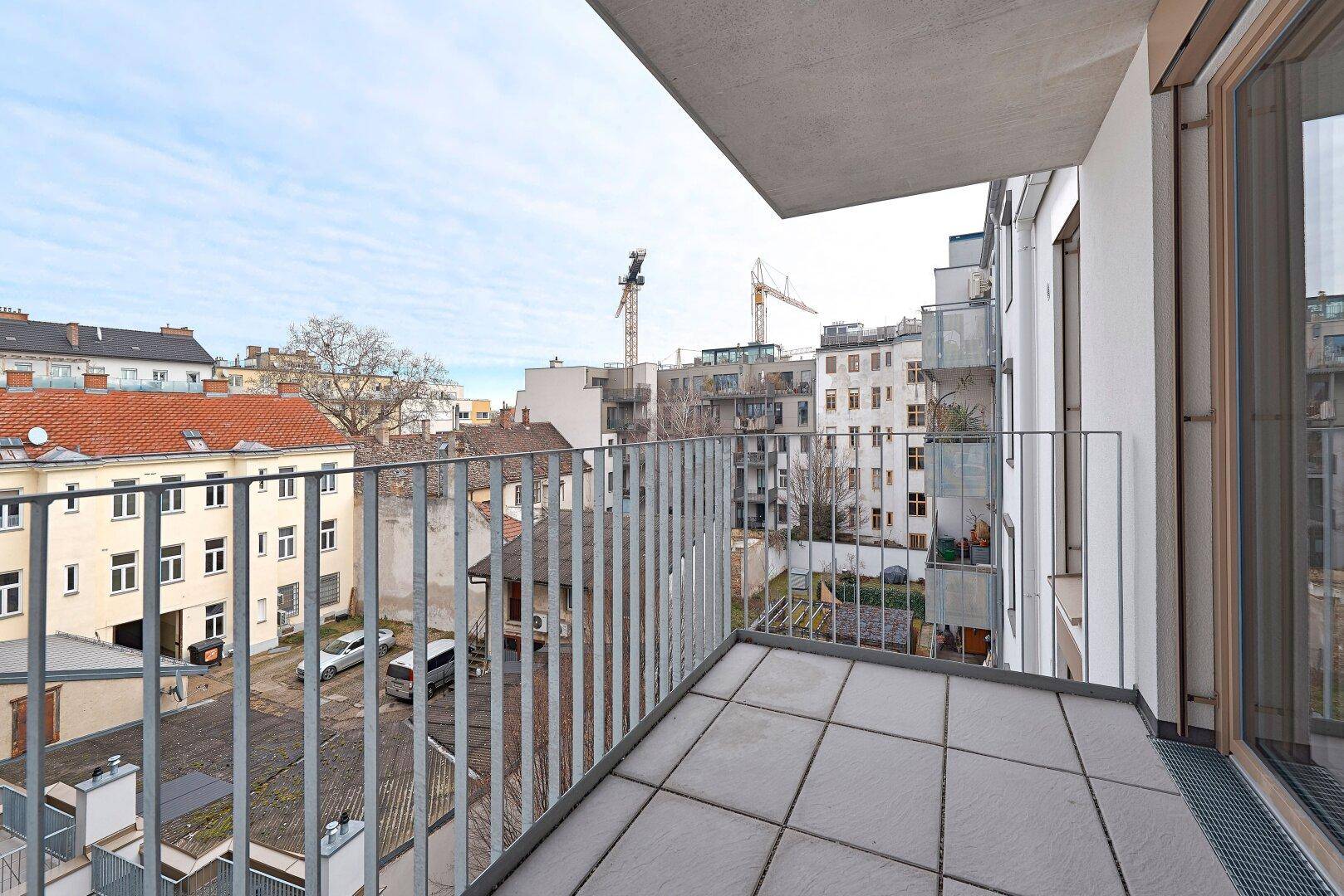 Balkon mit Fliesenboden und Blick auf die umliegende Stadtbebauung und Baustellenkräne.