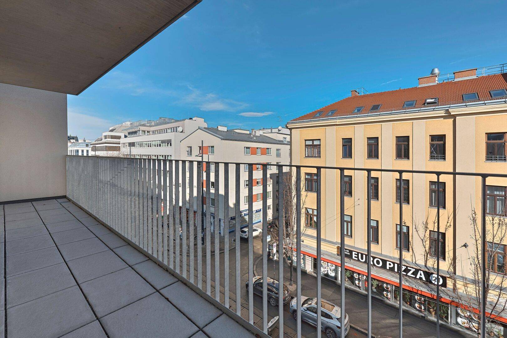 Balkon mit Fliesenboden und Blick auf die belebte Straße und die gegenüberliegenden Gebäude.