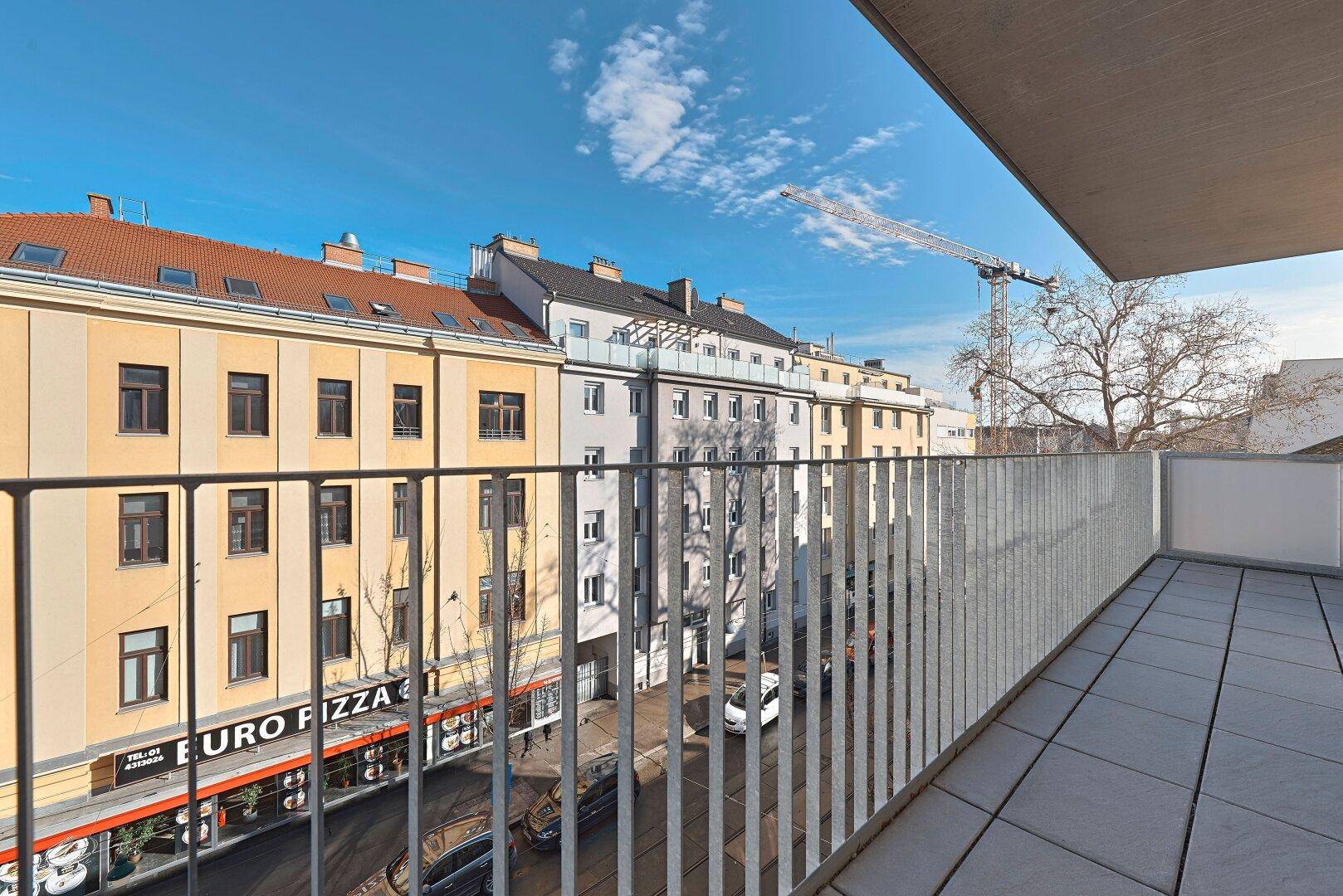 Heller Balkon mit Fliesenboden und Stadtblick, inklusive eines Baukrans in der Ferne.