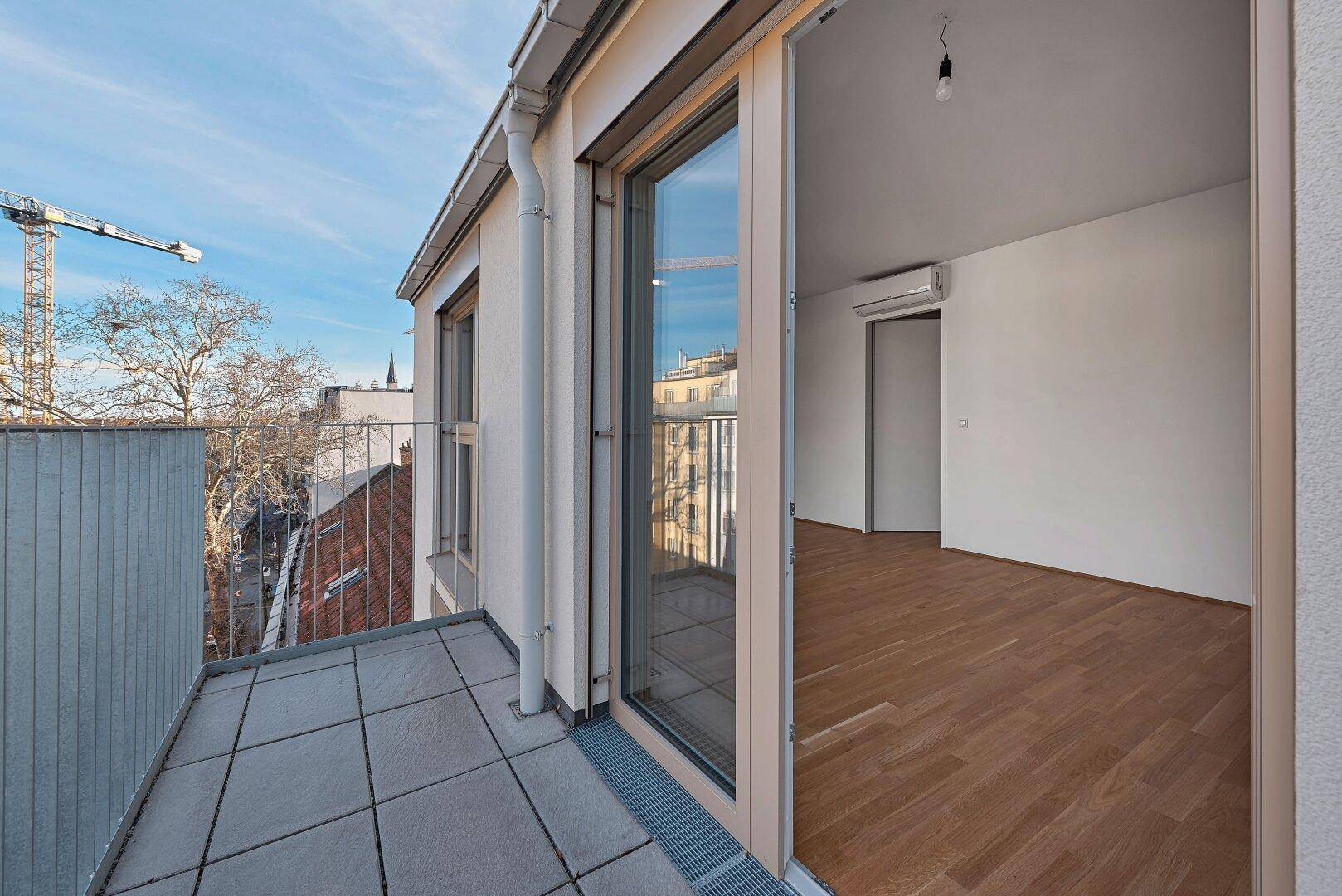 Balkon mit Fliesenboden und Blick auf die Stadt, verbunden mit einem hellen Innenraum.