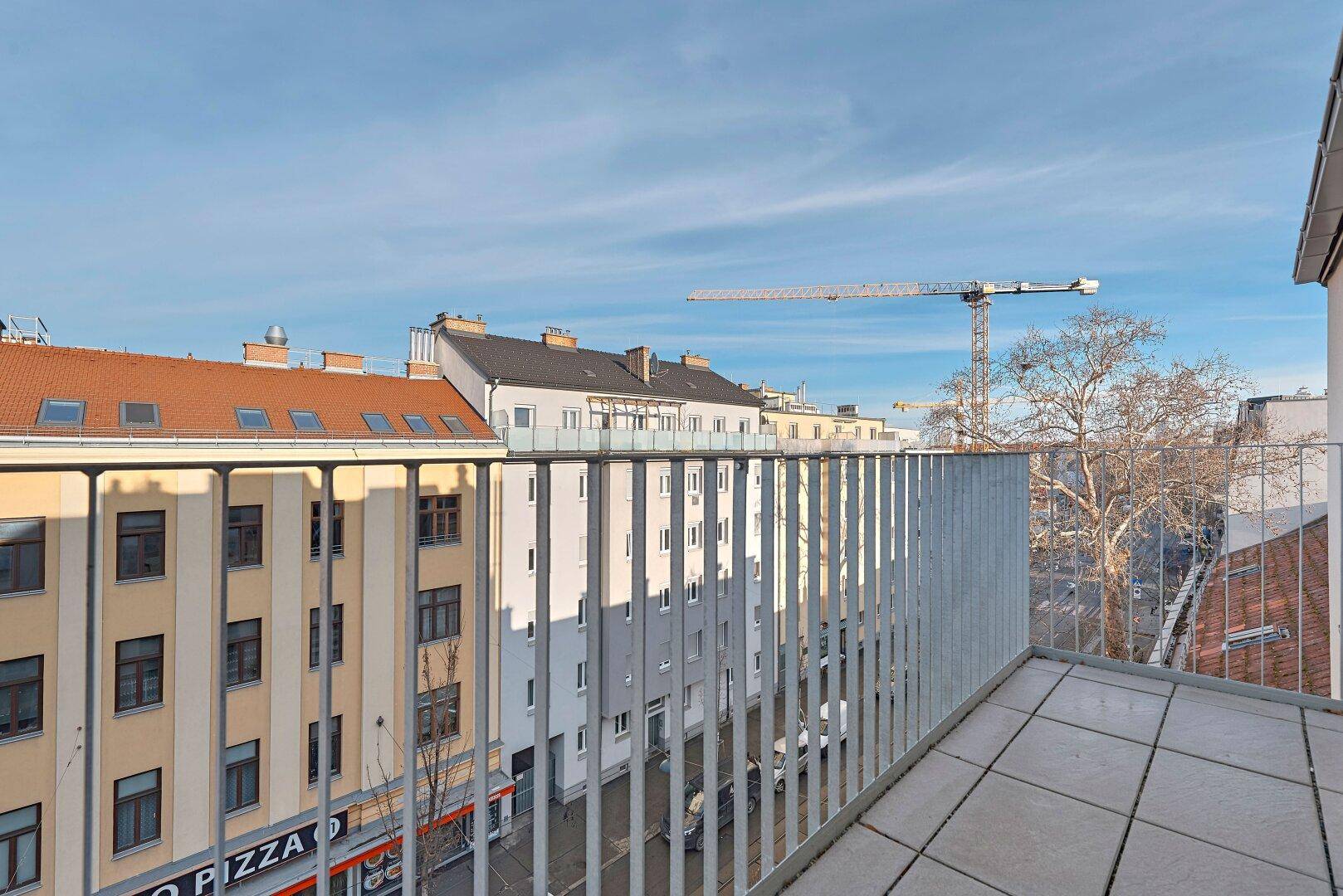 Geräumiger Balkon mit Fliesenboden und Blick auf die umliegenden Gebäude und die Stadt.
