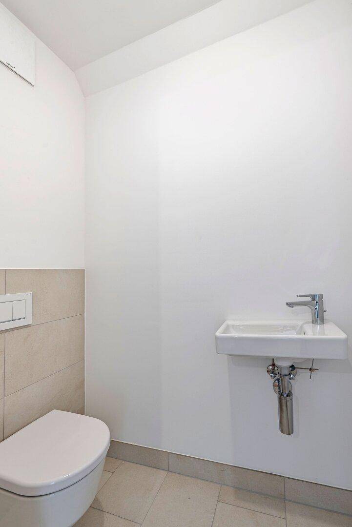 Modernes Gäste-WC mit wandmontierter Toilette und kleinem Waschbecken.