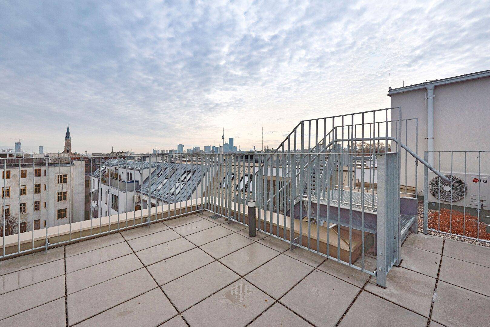 Geräumige Dachterrasse mit Fliesenboden und Metallgeländer, bietet einen weiten Stadtblick.