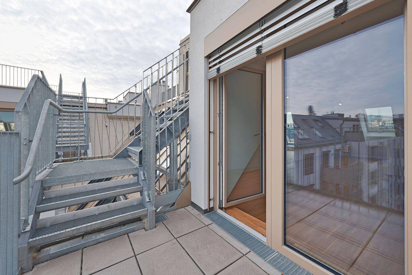 Dachterrasse mit Zugang durch eine große Glasschiebetür und Metalltreppe zu einer weiteren Ebene.