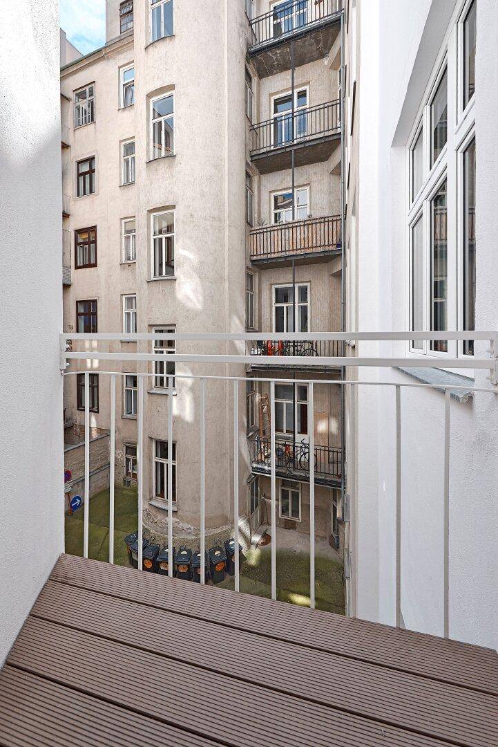 Kleiner Balkon mit Holzboden und Blick auf den ruhigen Innenhof des Gebäudes.
