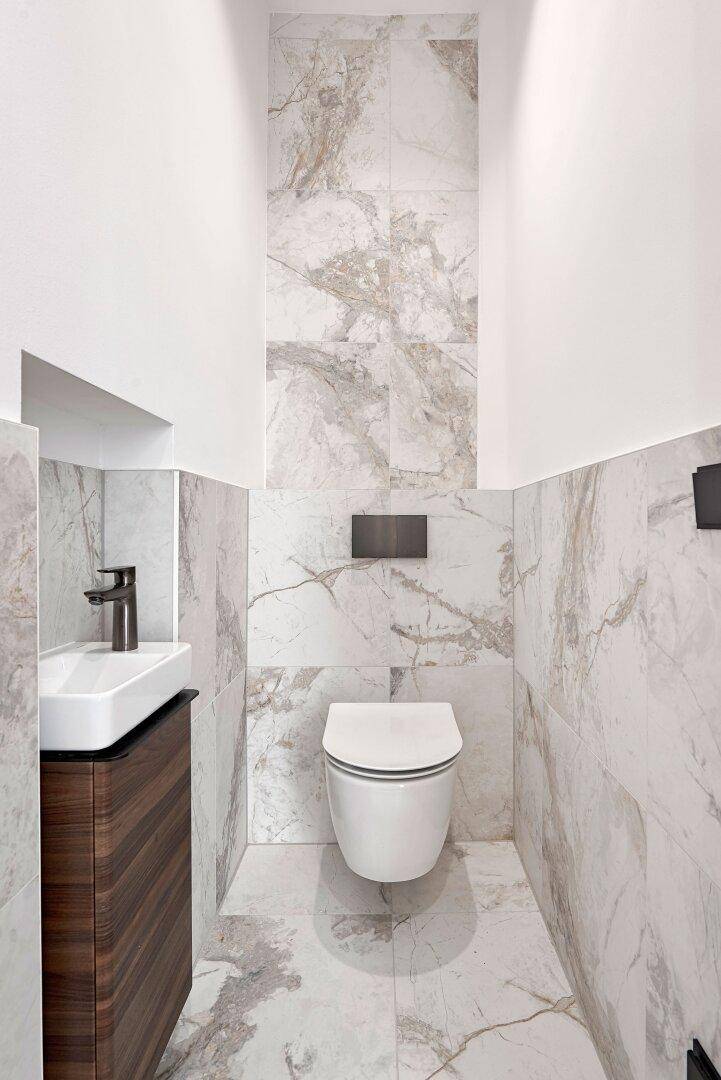 Modernes Gäste-WC mit wandhängender Toilette, kleinem Waschtisch und stilvollen Marmorfliesen.