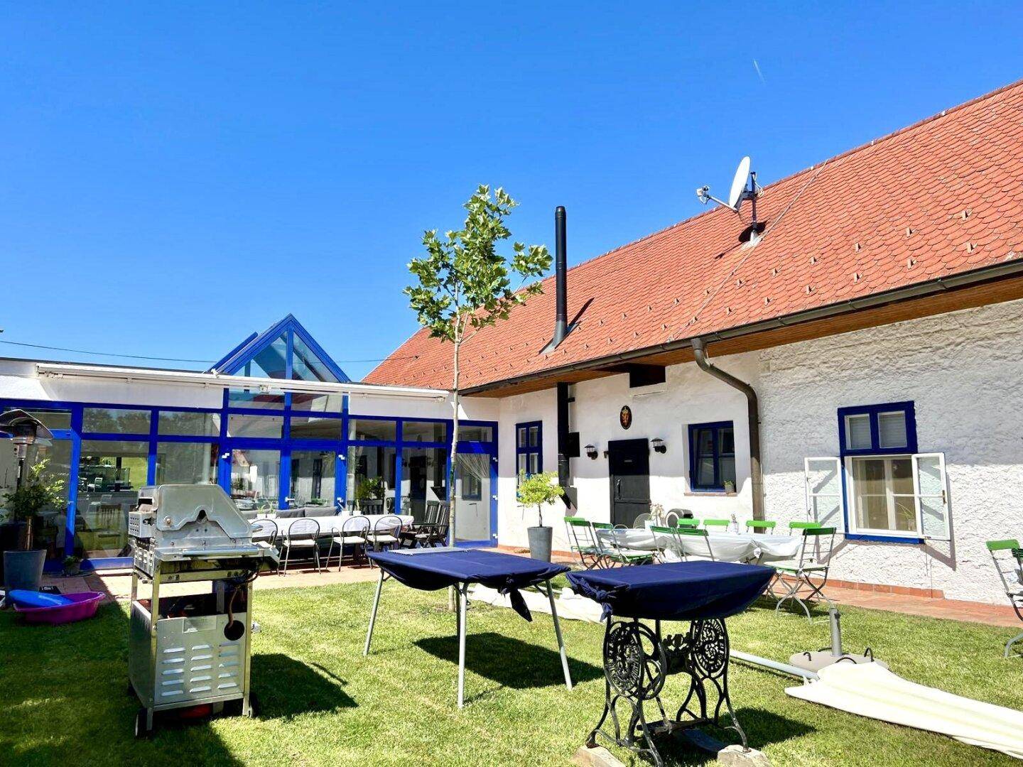 Hinterhof mit Rasenfläche, Grill und einem großen Wintergarten mit blauen Fensterrahmen.