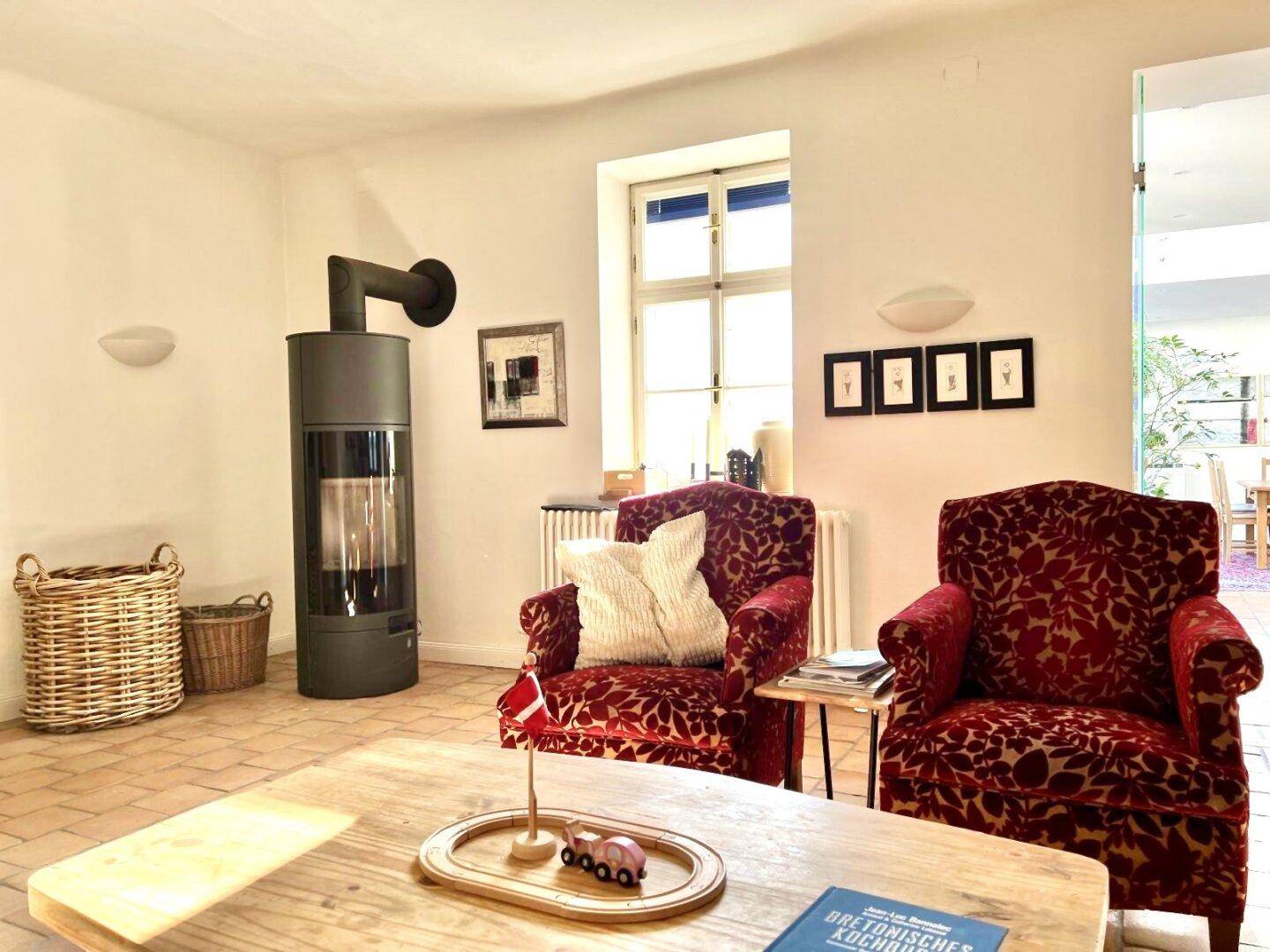 Gemütliches Wohnzimmer mit Terrakottaboden, Kaminofen und zwei roten Polstersesseln.